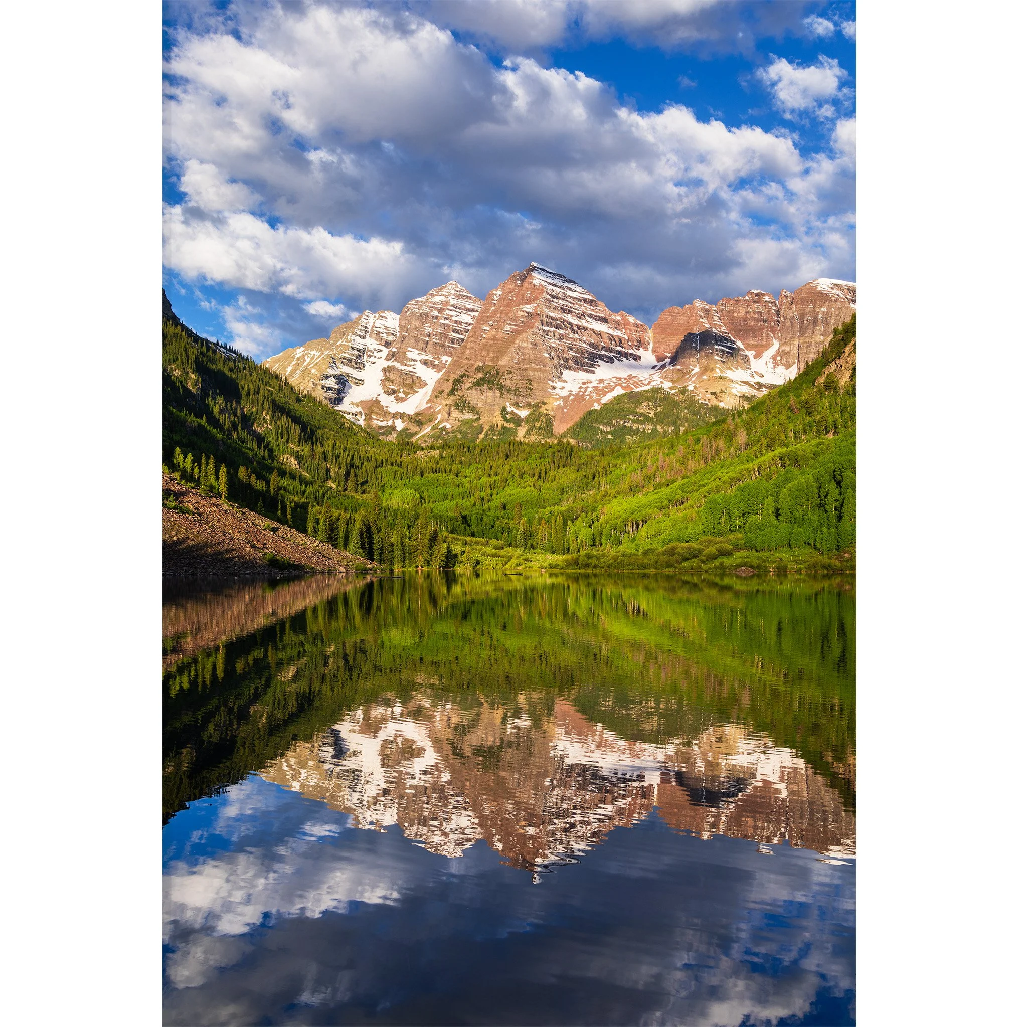 Maroon Bells reflected in the still water of Maroon Lake with green spring aspen and snow on the peaks, Colorado.