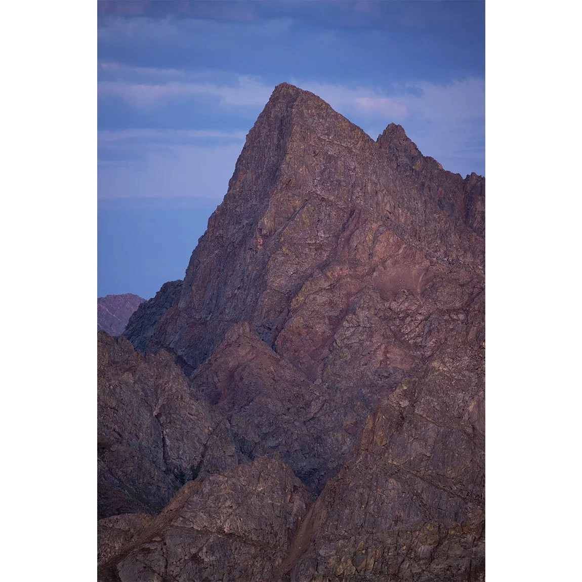 Close-up view of Peak C in the Gore Range of Colorado captured in twilight after sunset, showing rugged alpine rock glowing faintly in soft purple and blue evening light.