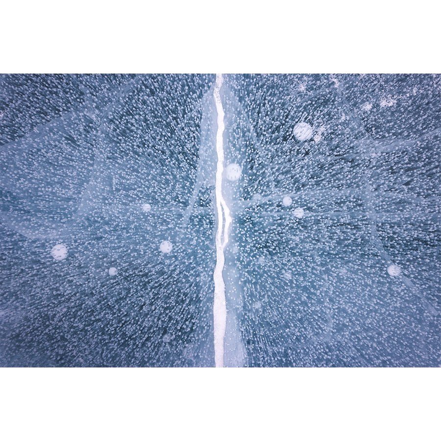Aerial view of a frozen lake in Estes Park with a large central crack and trapped methane bubbles forming abstract, radial patterns in the ice.