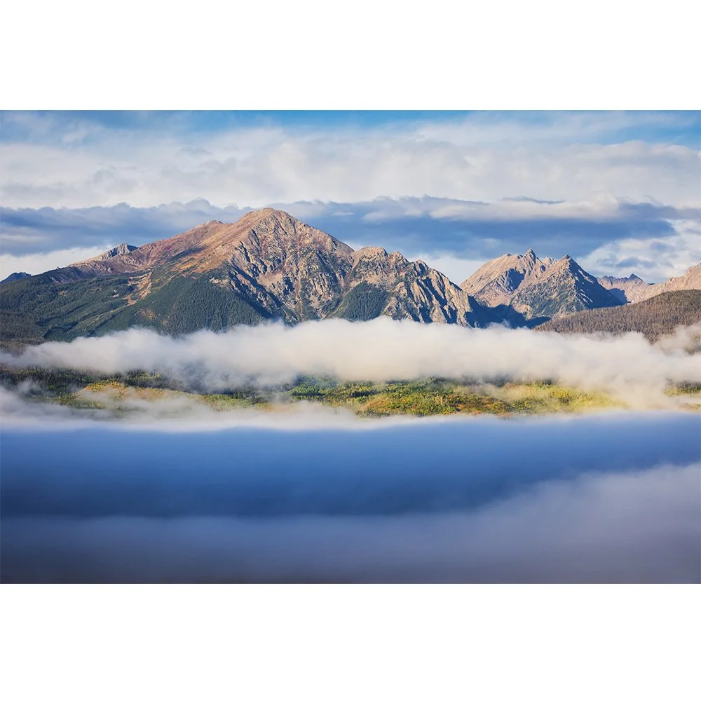 Peaks of the Gore Range seen from Ute Pass in Summit County, Colorado, rising above layers of morning fog with sunlight illuminating alpine ridges and forested slopes.