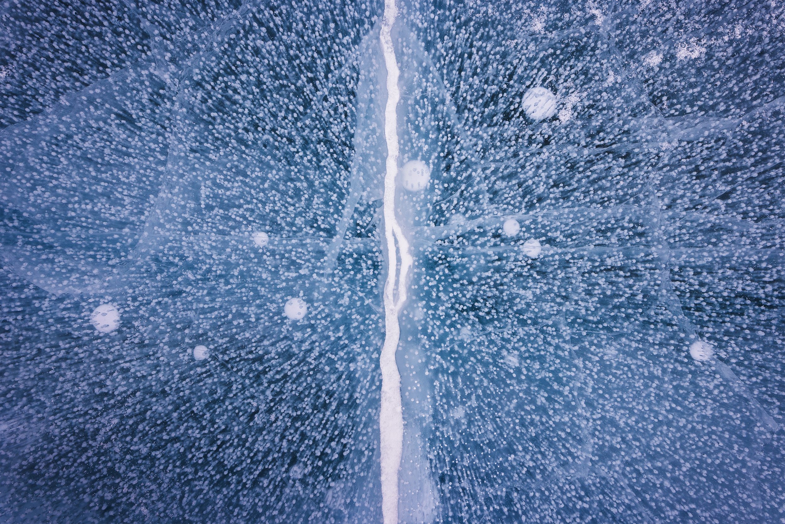 A bird's eye view of a wet, icy road with a white dividing line running down the center and water droplets scattered across the surface.
