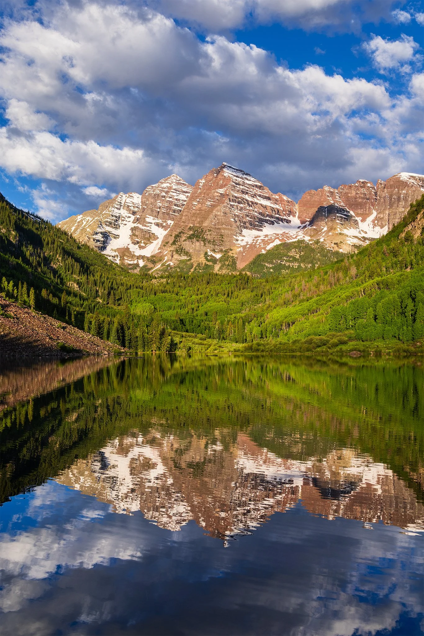The Maroon Bells reflected in the still water of Maroon Lake in early summer near Aspen, Colorado.