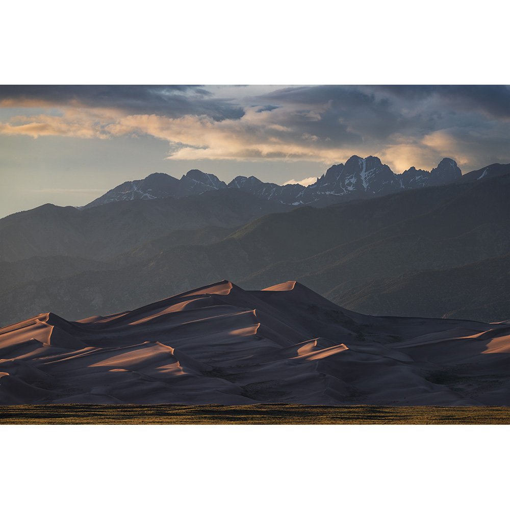 Sunset side-light striking the tallest sand dunes in North America in Colorado, with 14,000-foot mountains in the background.