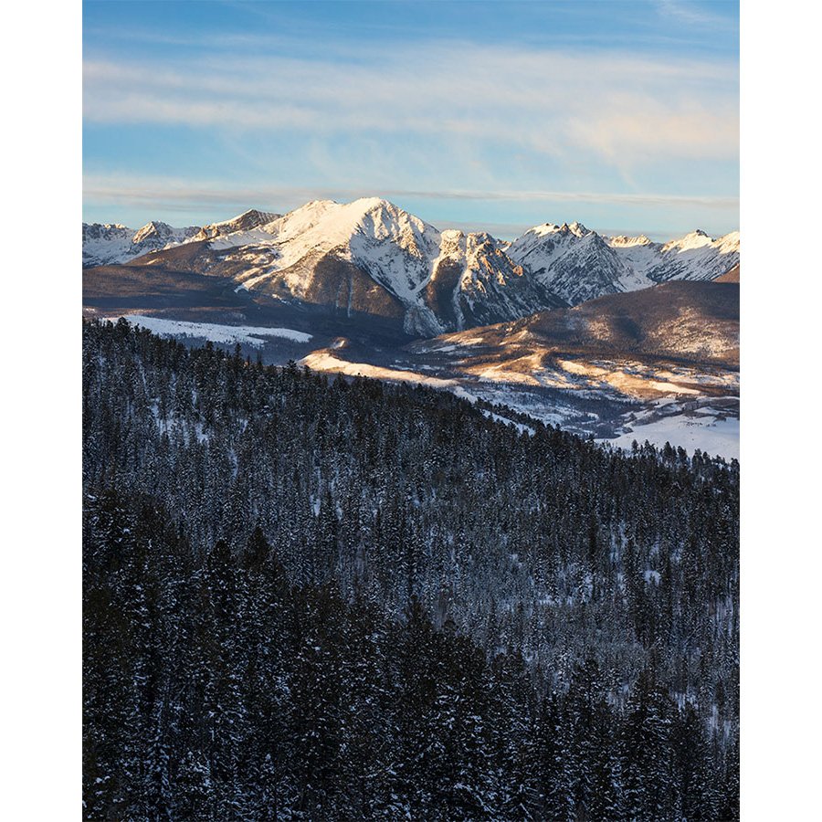 Snow-covered Gore Range seen from Ute Pass near Silverthorne, Colorado on a crisp winter morning, with sunlit valleys and frosted pine forests.