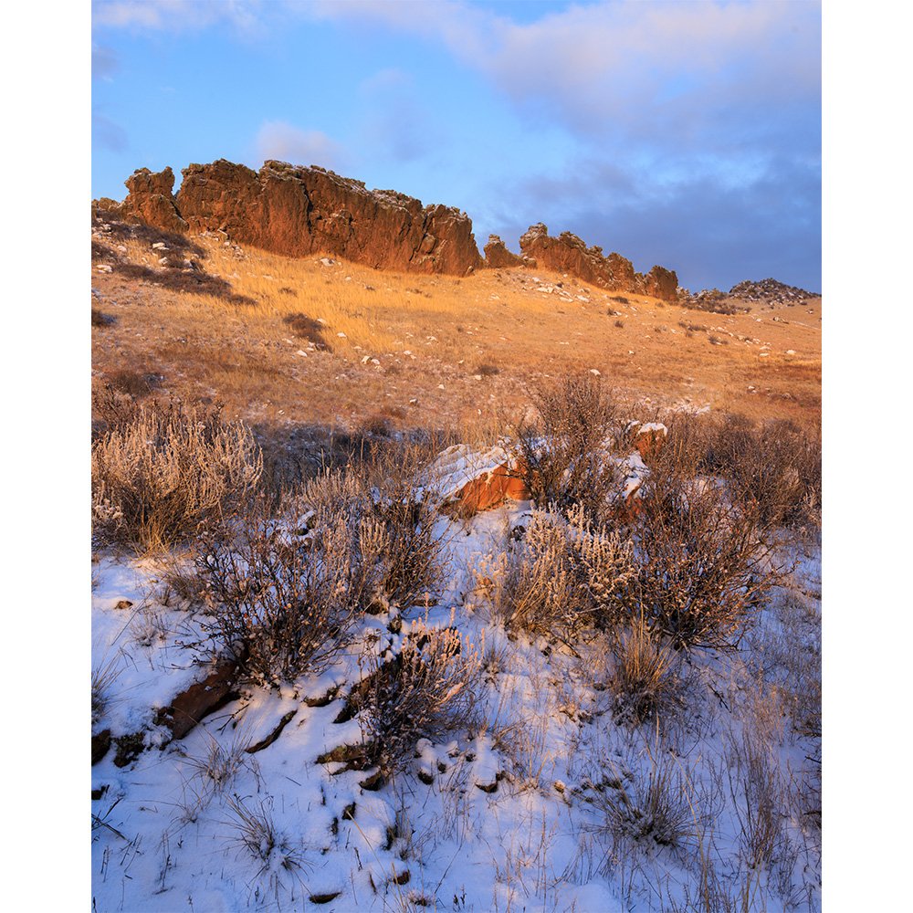 Early morning sunlight glows on the rock formations of Devil’s Backbone near Loveland, Colorado, with snow-covered sagebrush and grasses in the foreground.