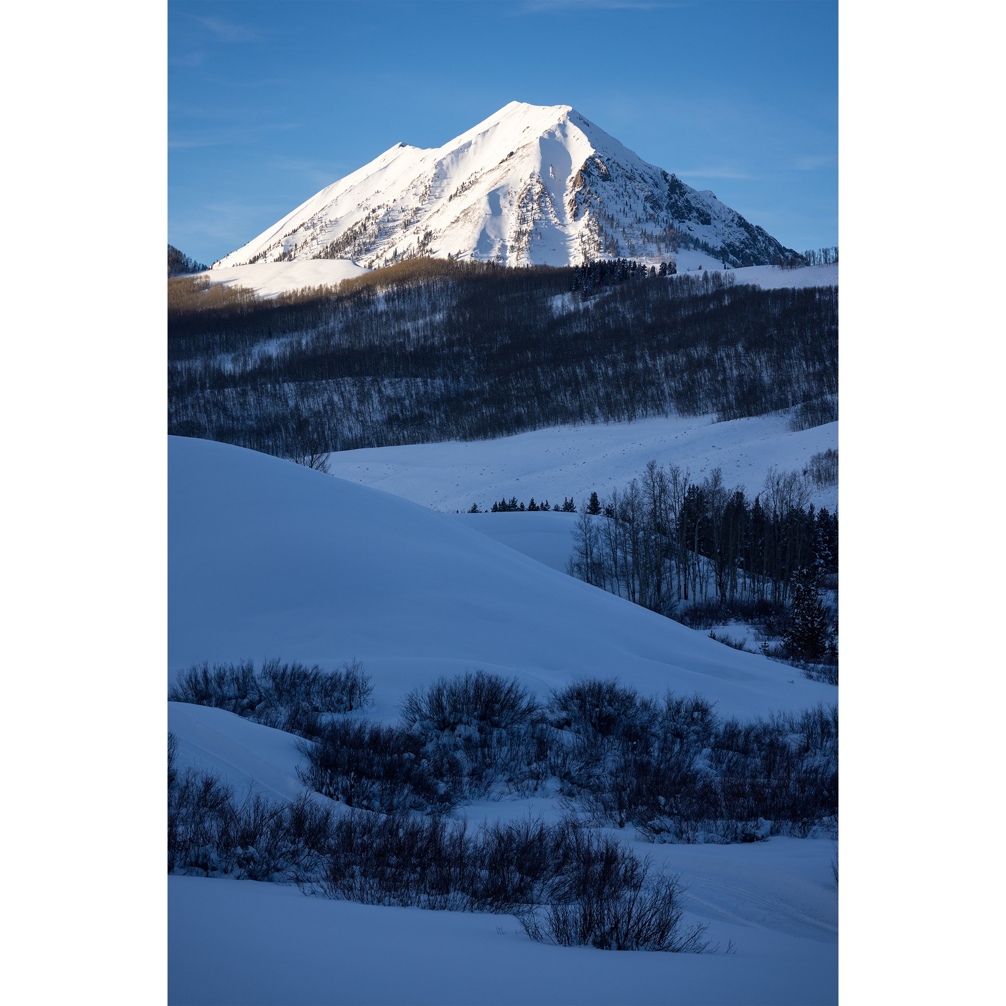 Gothic Mountain lit by evening sun above a snow-covered valley near Crested Butte, Colorado, in winter.