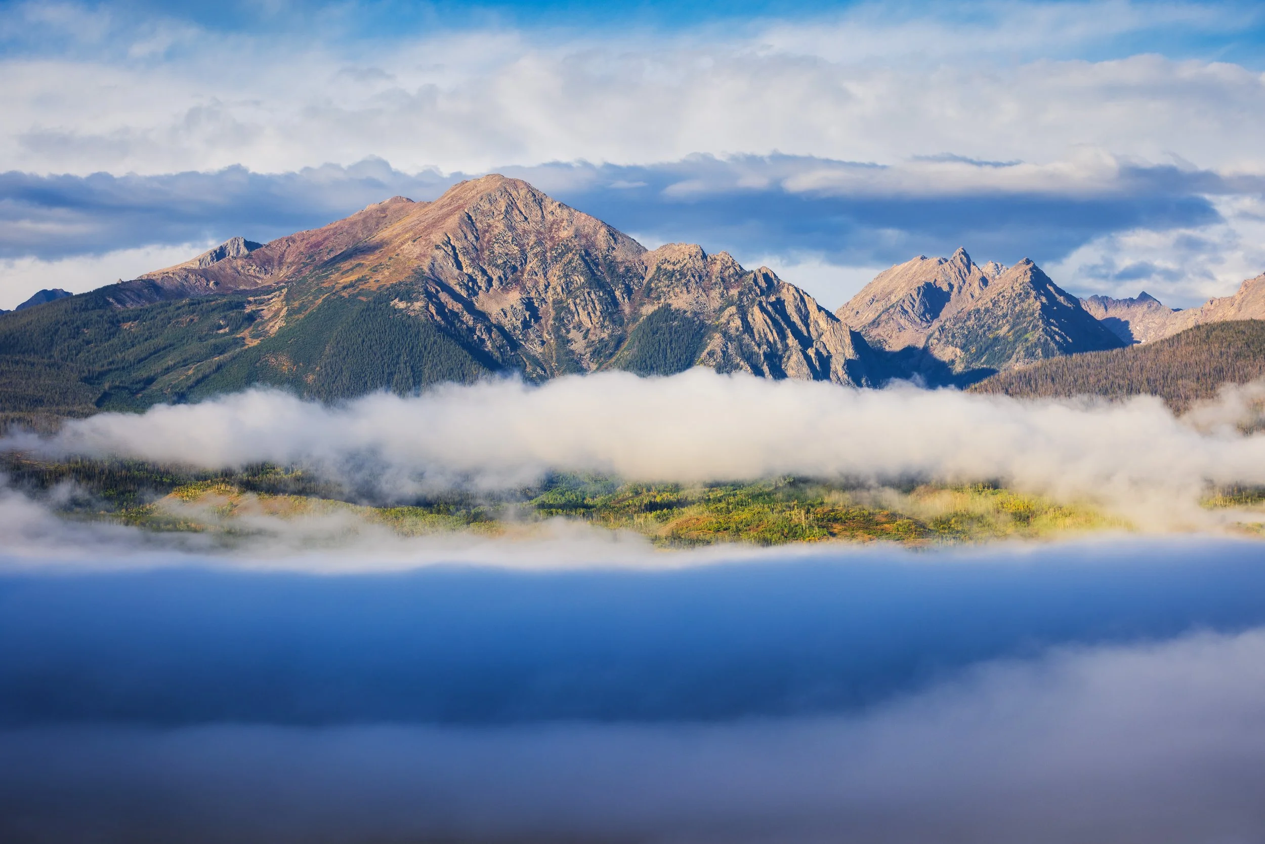 A mountain range with rocky peaks and green slopes, partly covered by clouds in the sky.