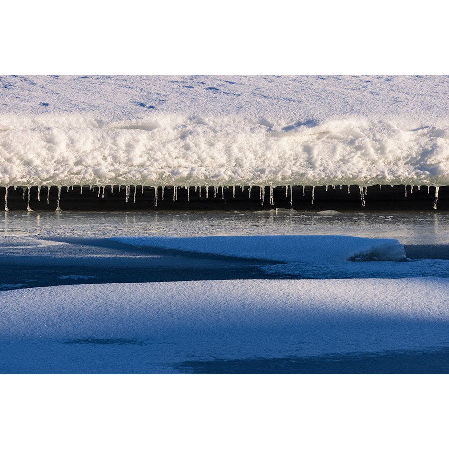 Icicles hang beneath a snow-covered ledge over the frozen surface of Lake Dillon, Colorado in winter light.