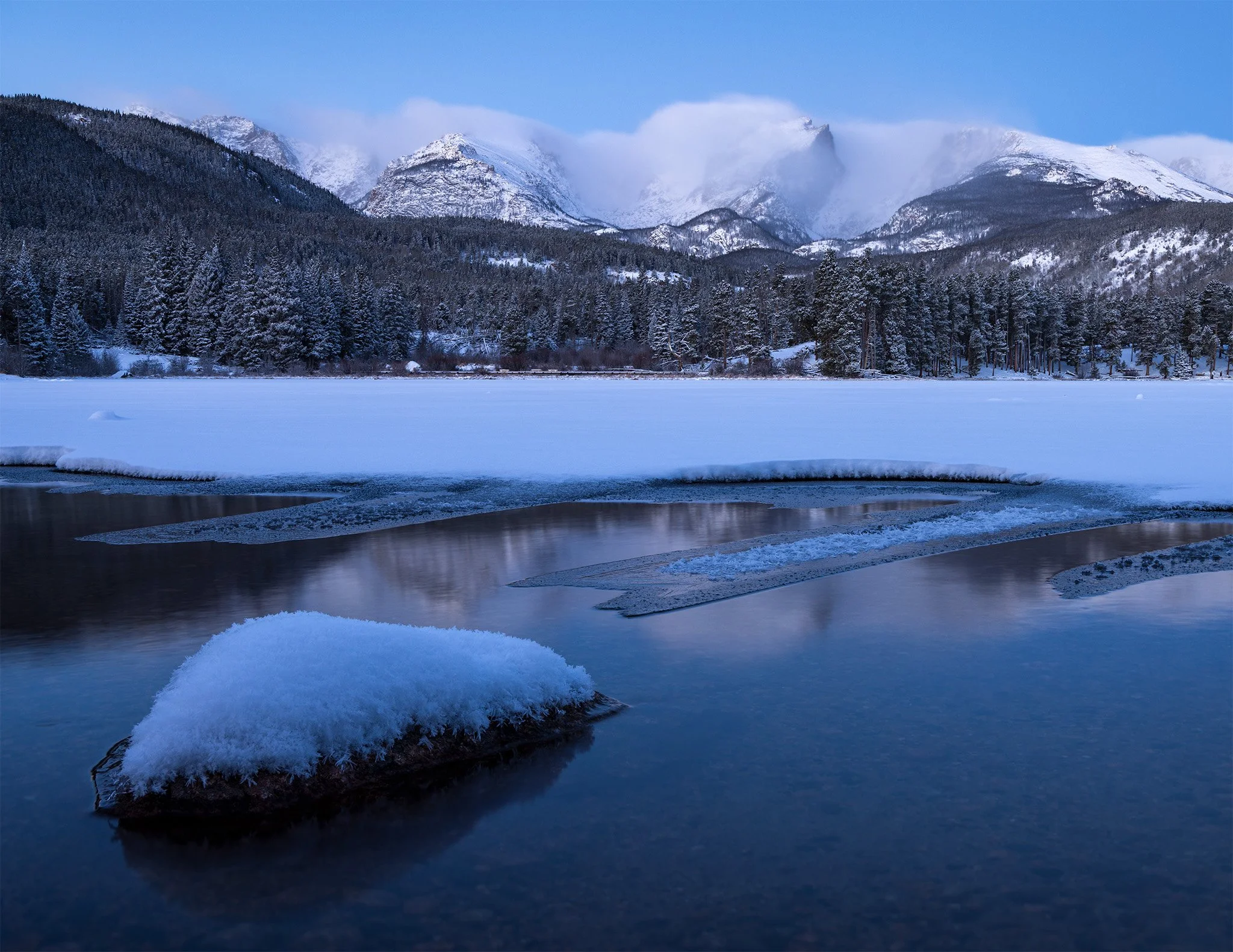Hallett Peak under cloud above a frozen Sprague Lake at blue hour, Rocky Mountain National Park, Colorado.
