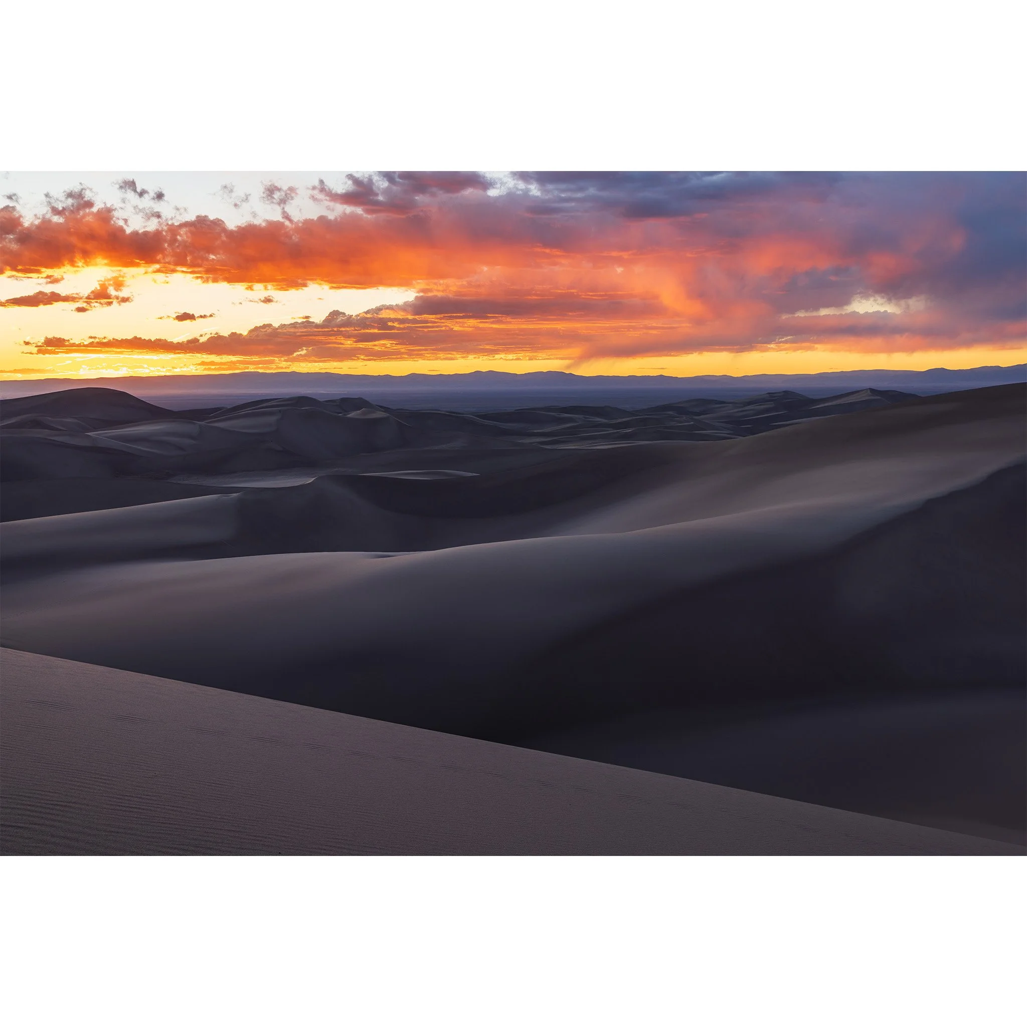 Orange and red sunset sky over the shadowed dunes at Great Sand Dunes National Park, San Luis Valley, Colorado.