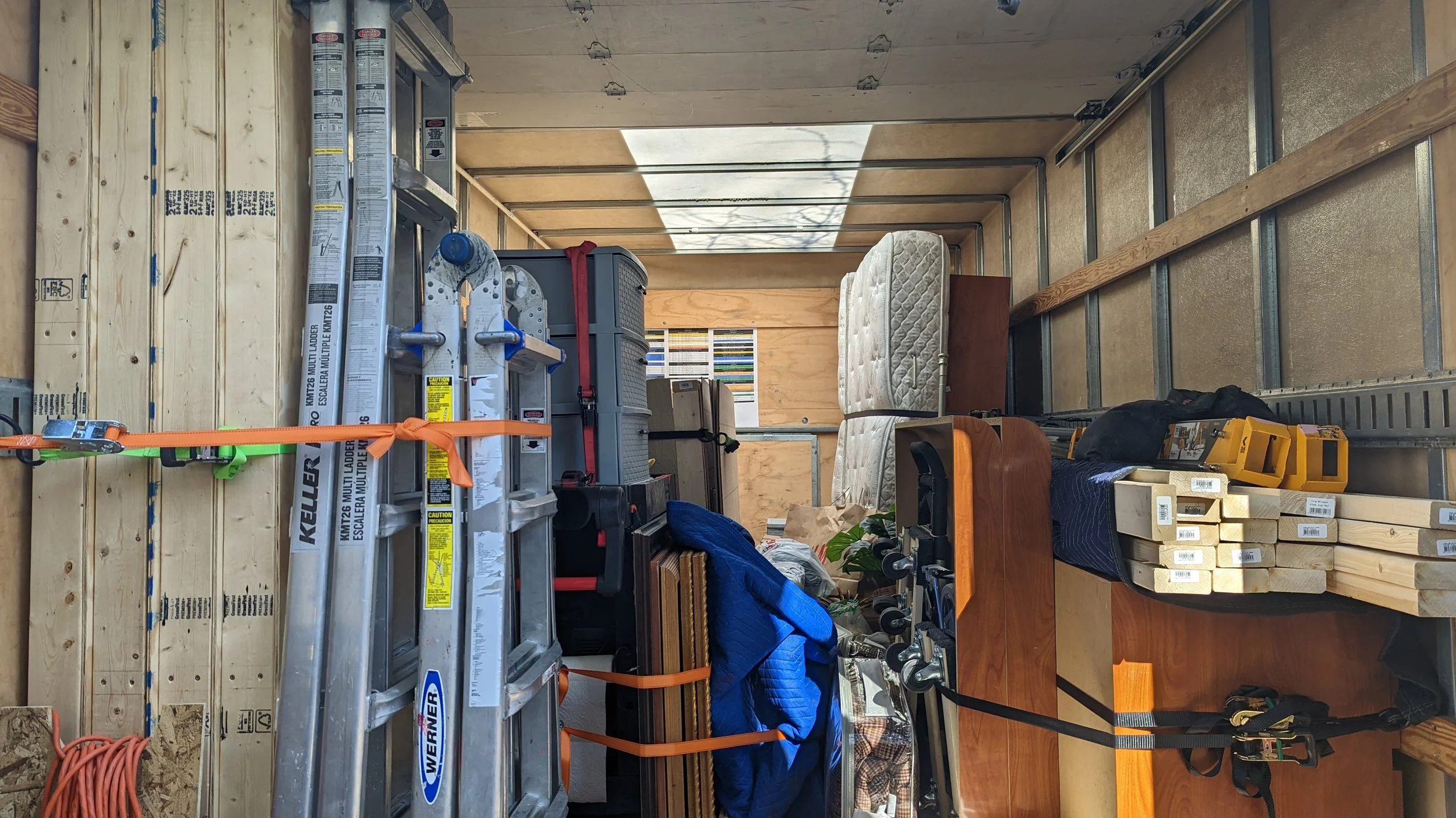 Construction site with wooden framing, a ladder, and various tools and supplies, including boxes and a mattress.