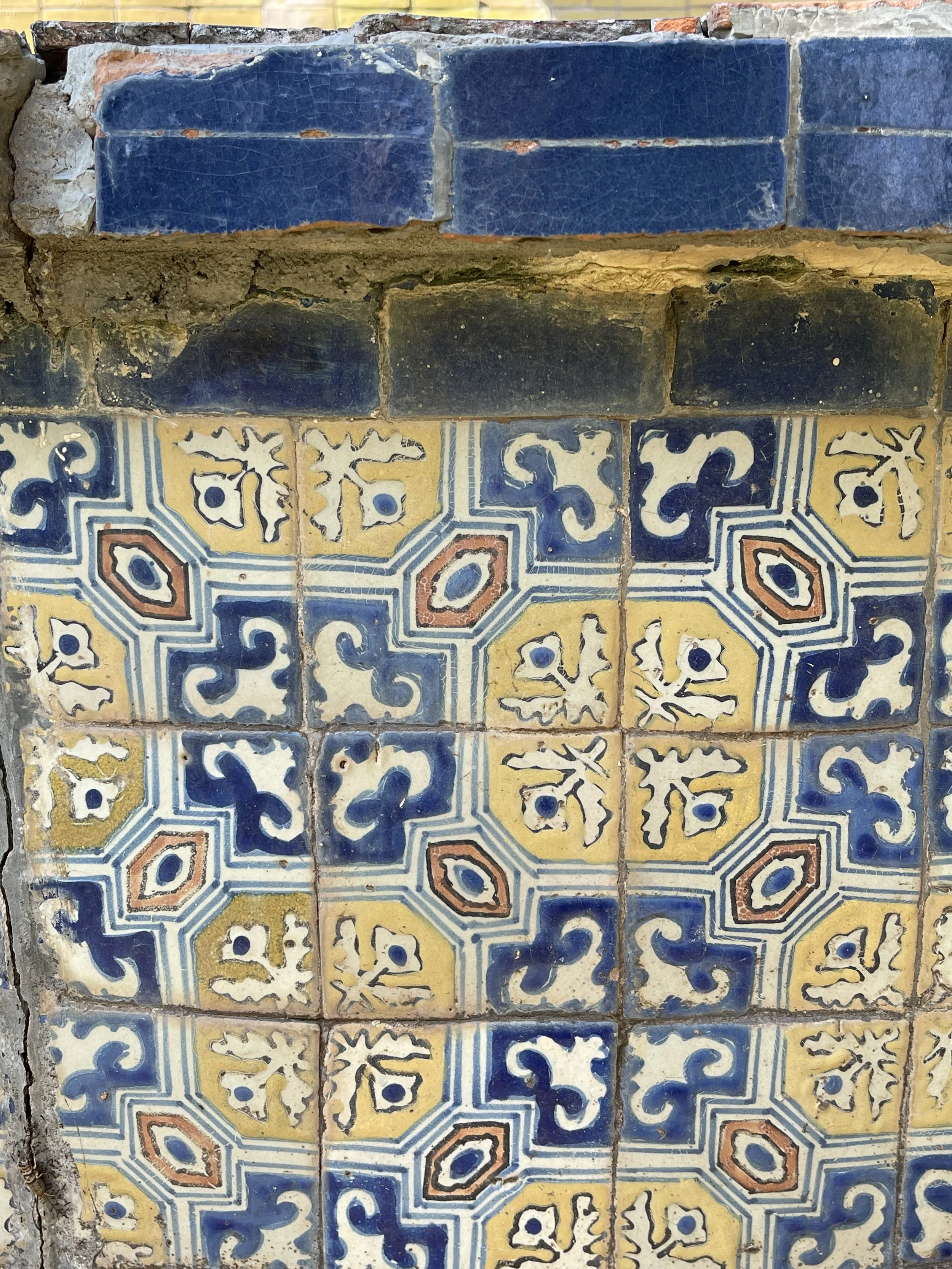 Colorful geometric pattern tiles with blue, yellow, and white designs on a wall.