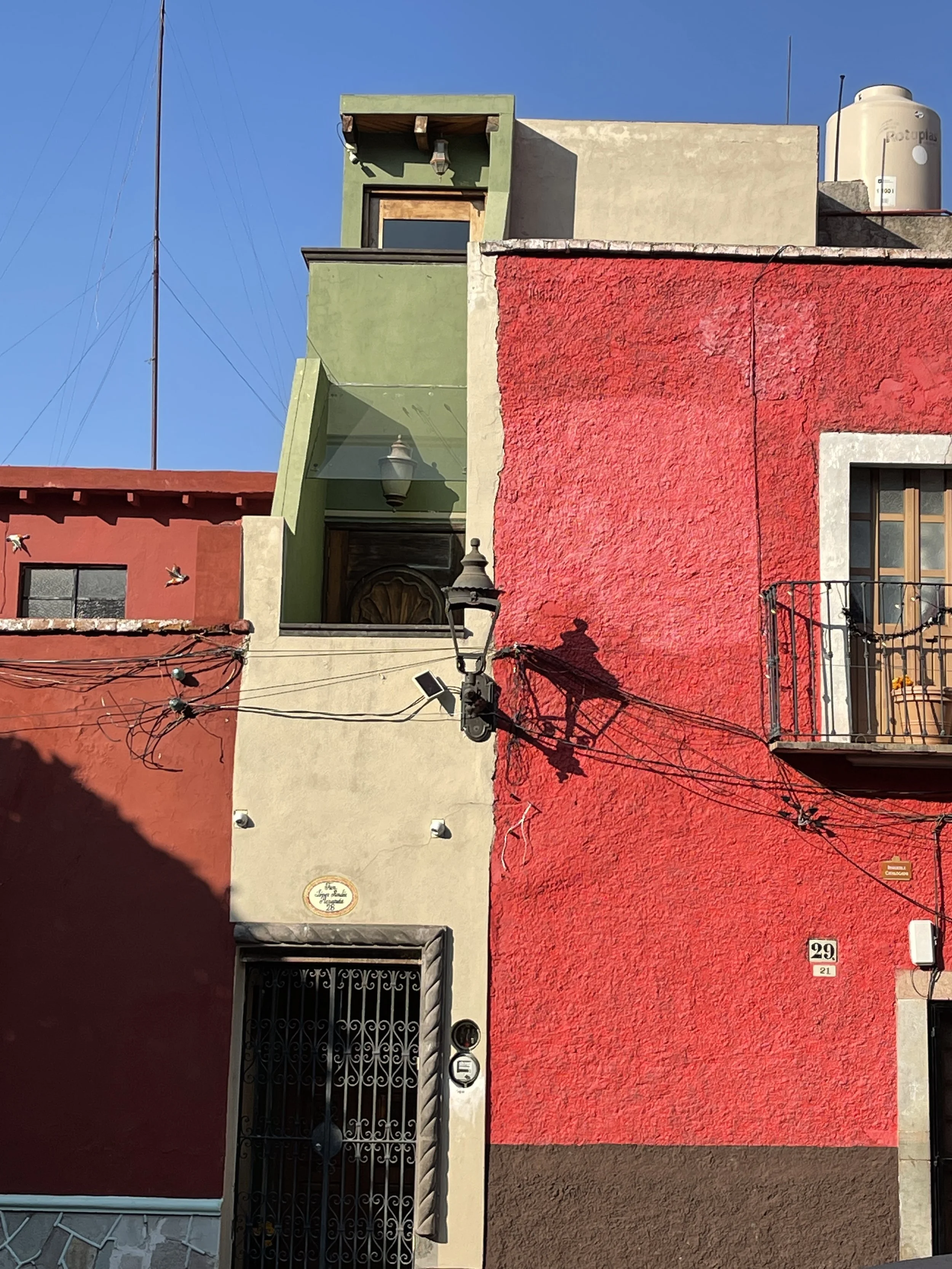 Colorful building exterior with red and green walls, wrought iron door, and balcony.