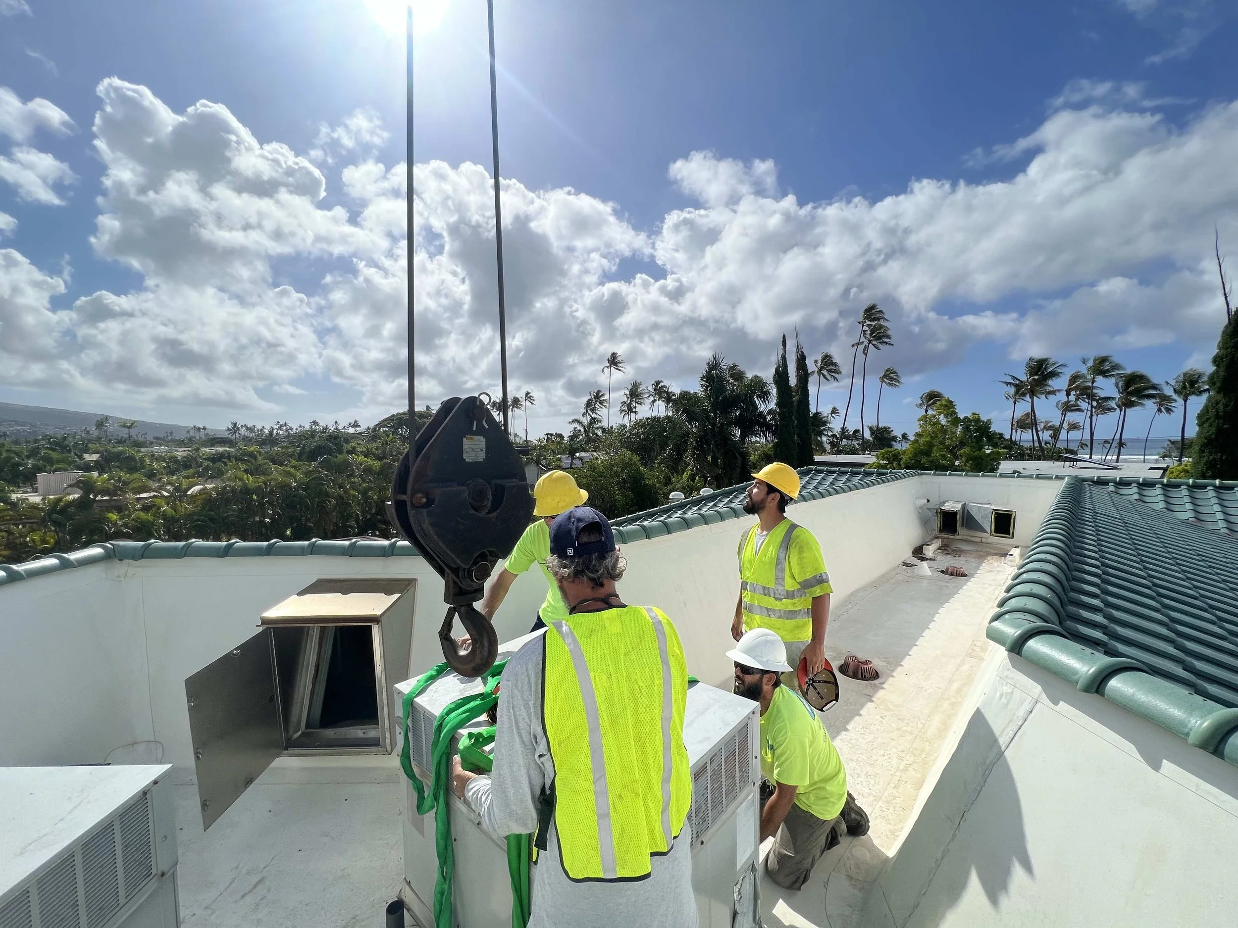Team of HVAC workers with crane lifting AC on roof.