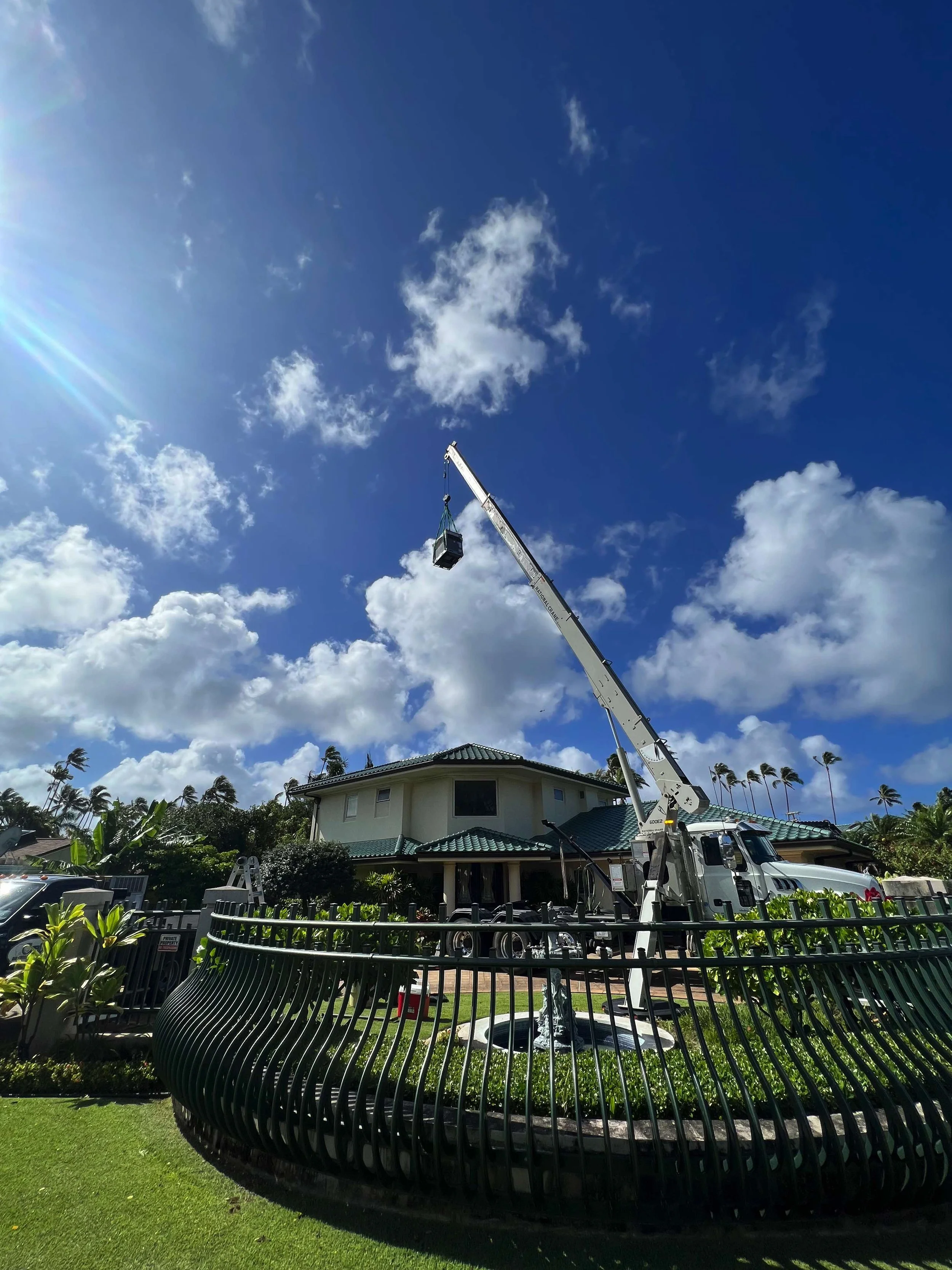 A new AC unit hoisted by a crane over a roof.