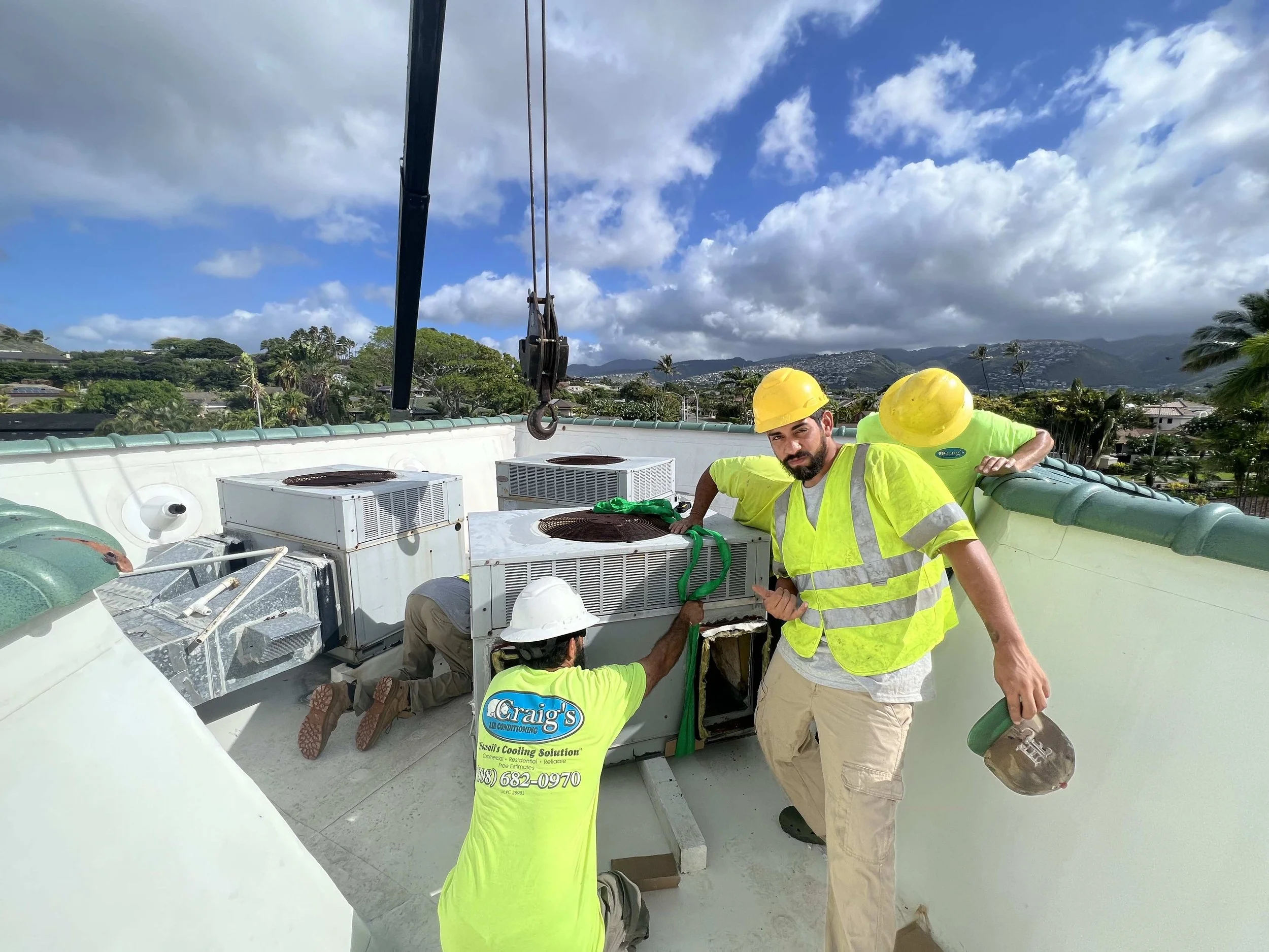 HVAC technicians removing an AC unit on a sunny rooftop.
