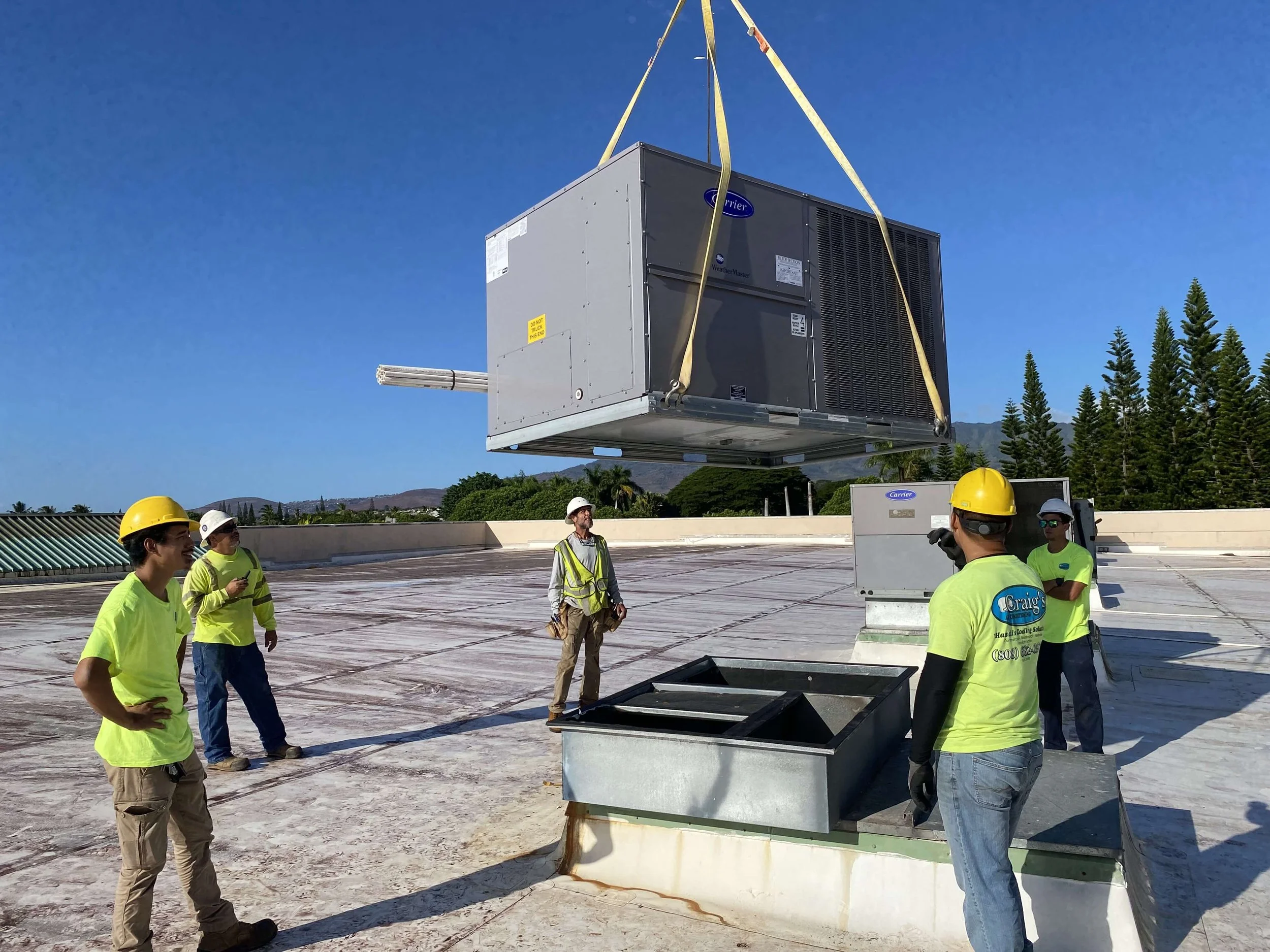 Technicians watch as a crane lowers a new HVAC system into place on a rooftop