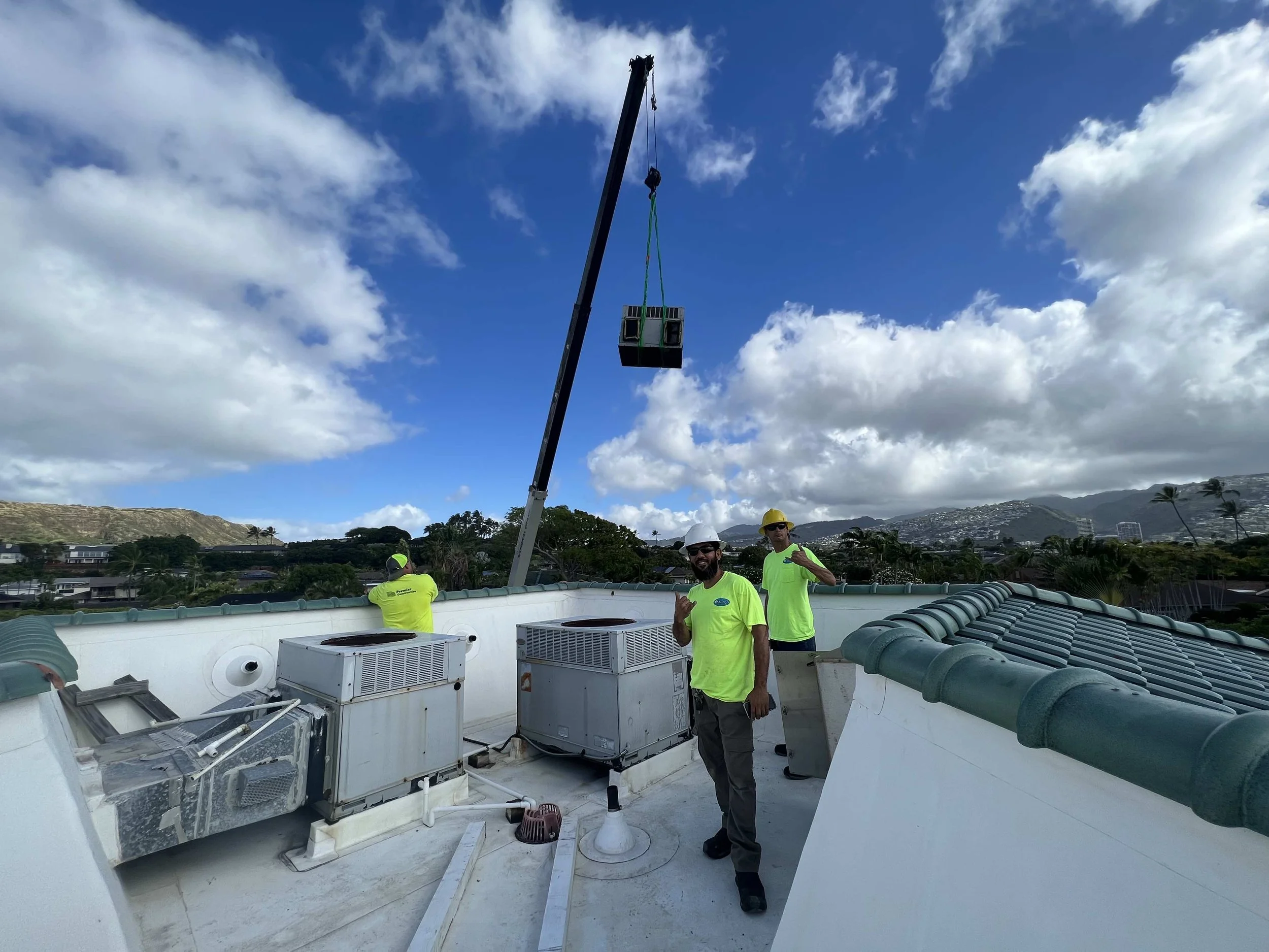 HVAC technicians pose in front of an AC unit with a crane on the rooftop.