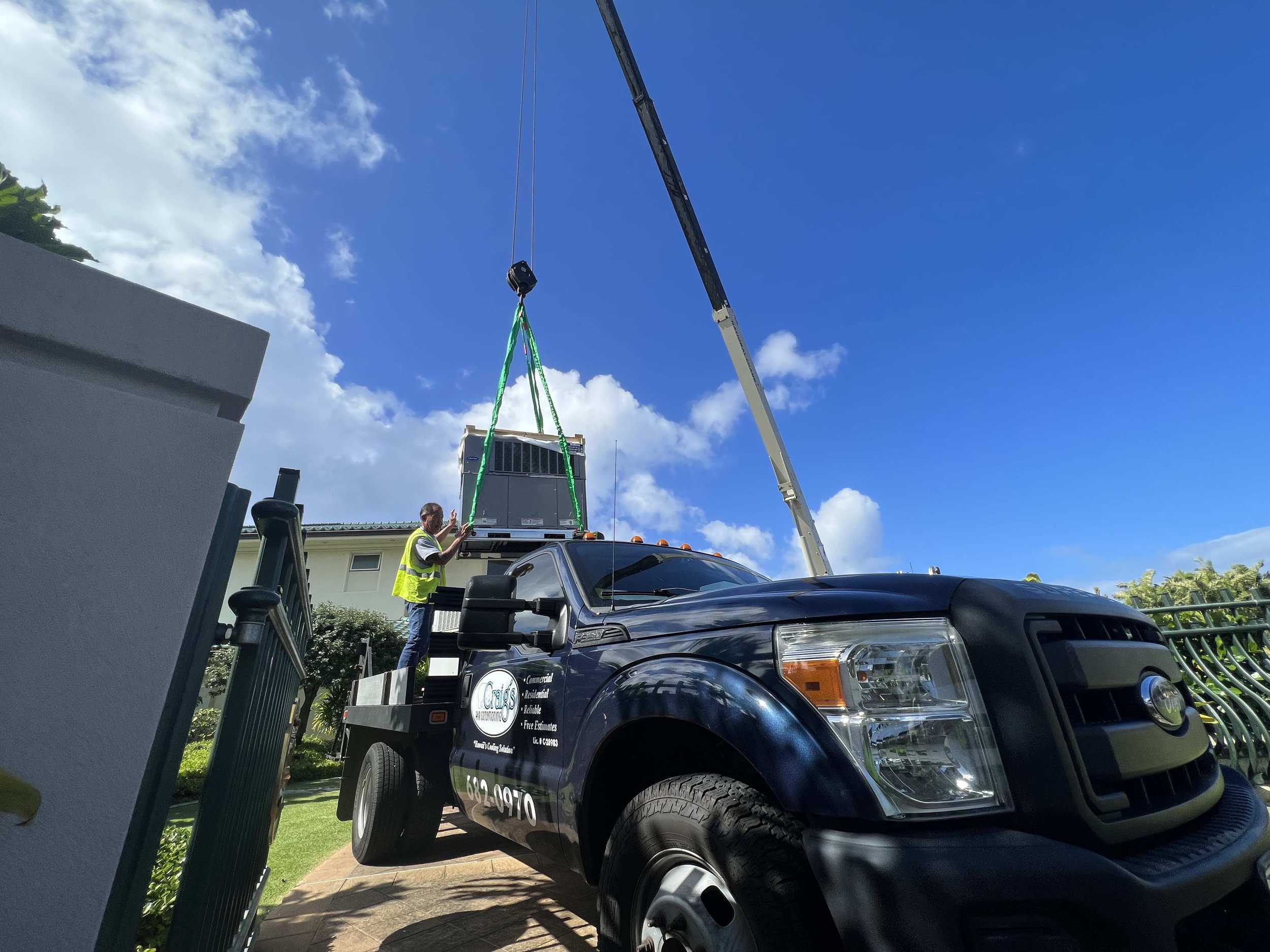 HVAC technician guiding a crane lifting an AC unit to the roof.