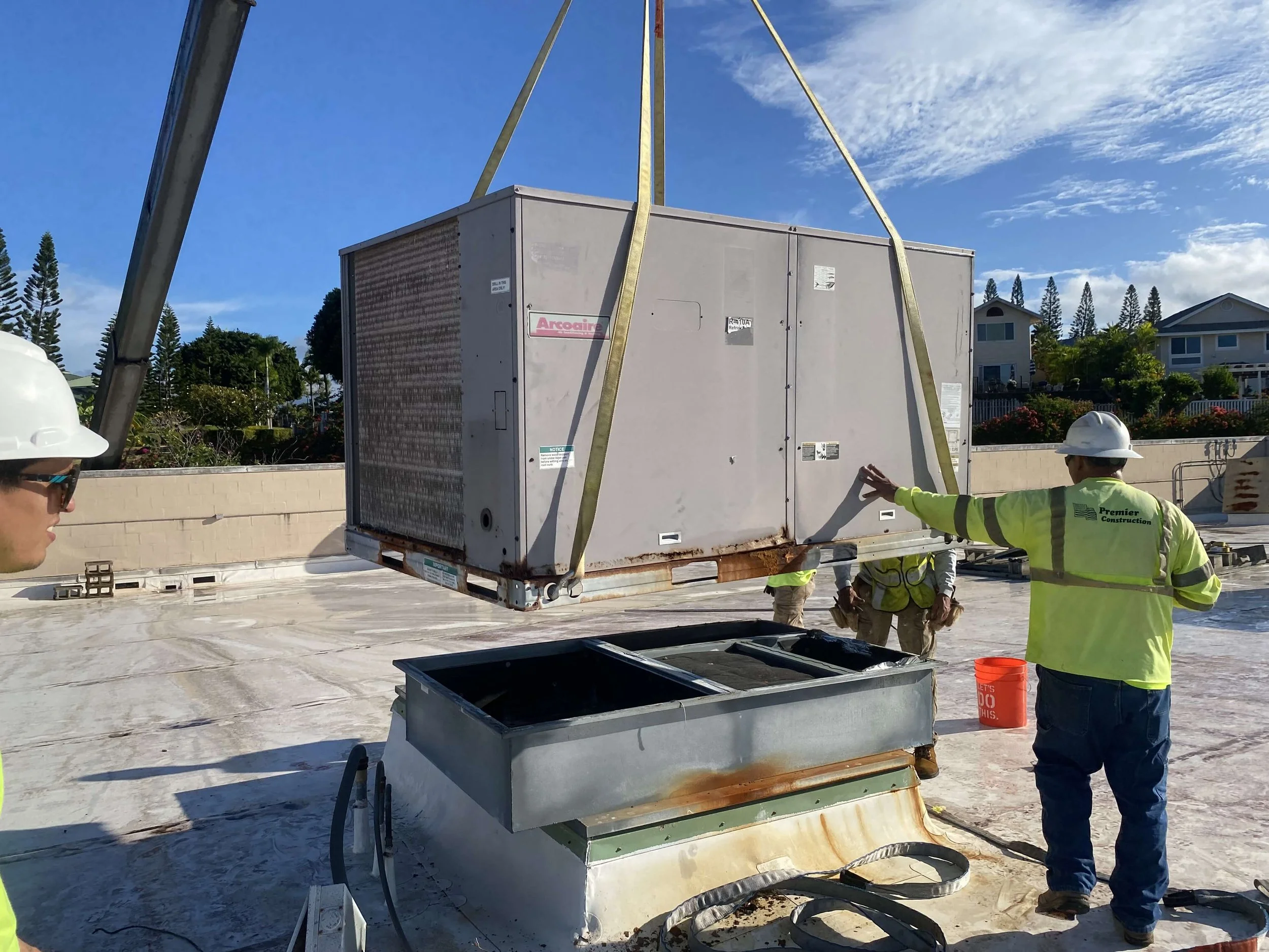 Technicians begin to lift an old HVAC unit off the rooftop with a crane, starting the removal process