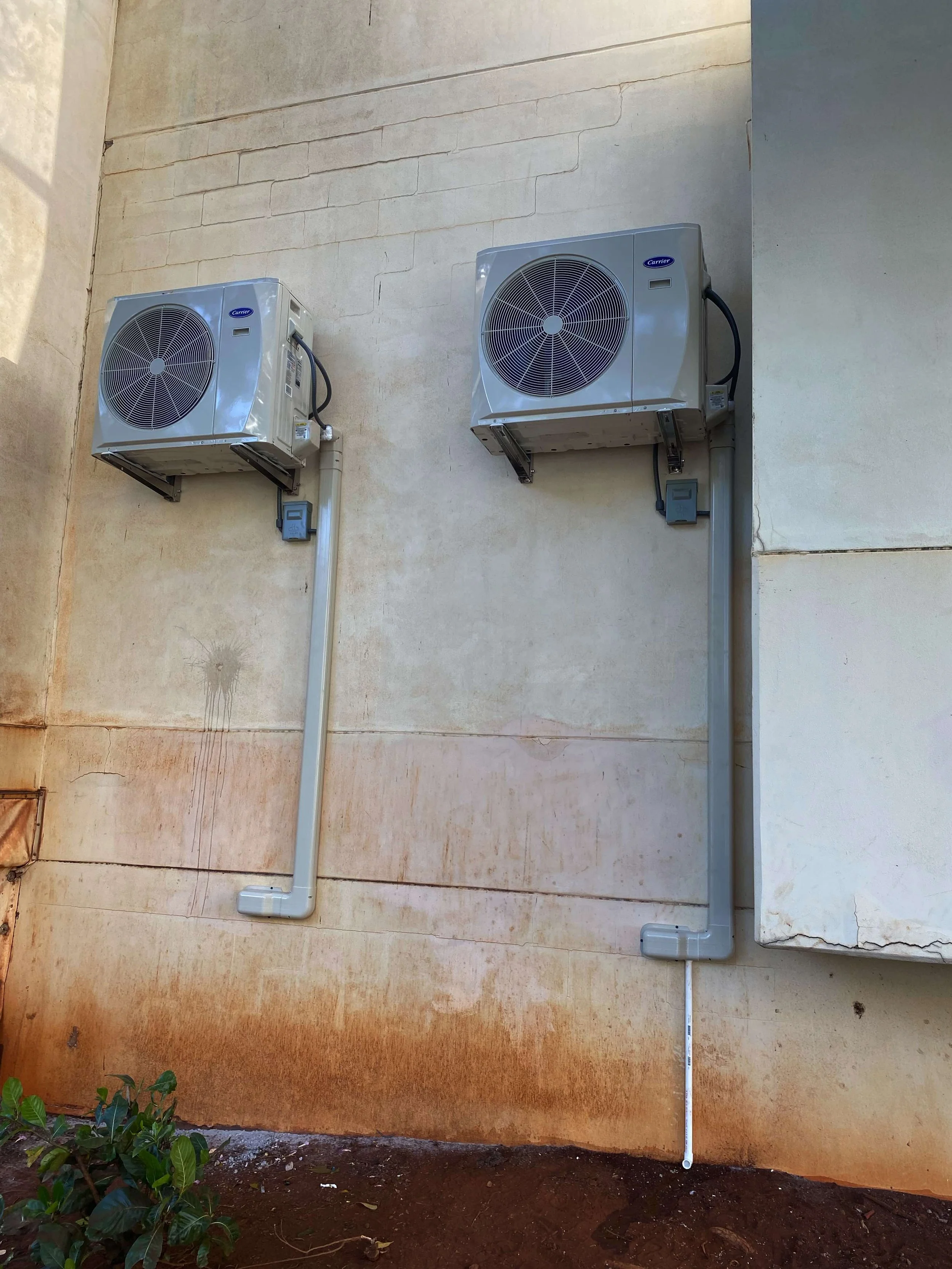Two outdoor AC units installed at ground level on an exterior wall, with visible conduit.