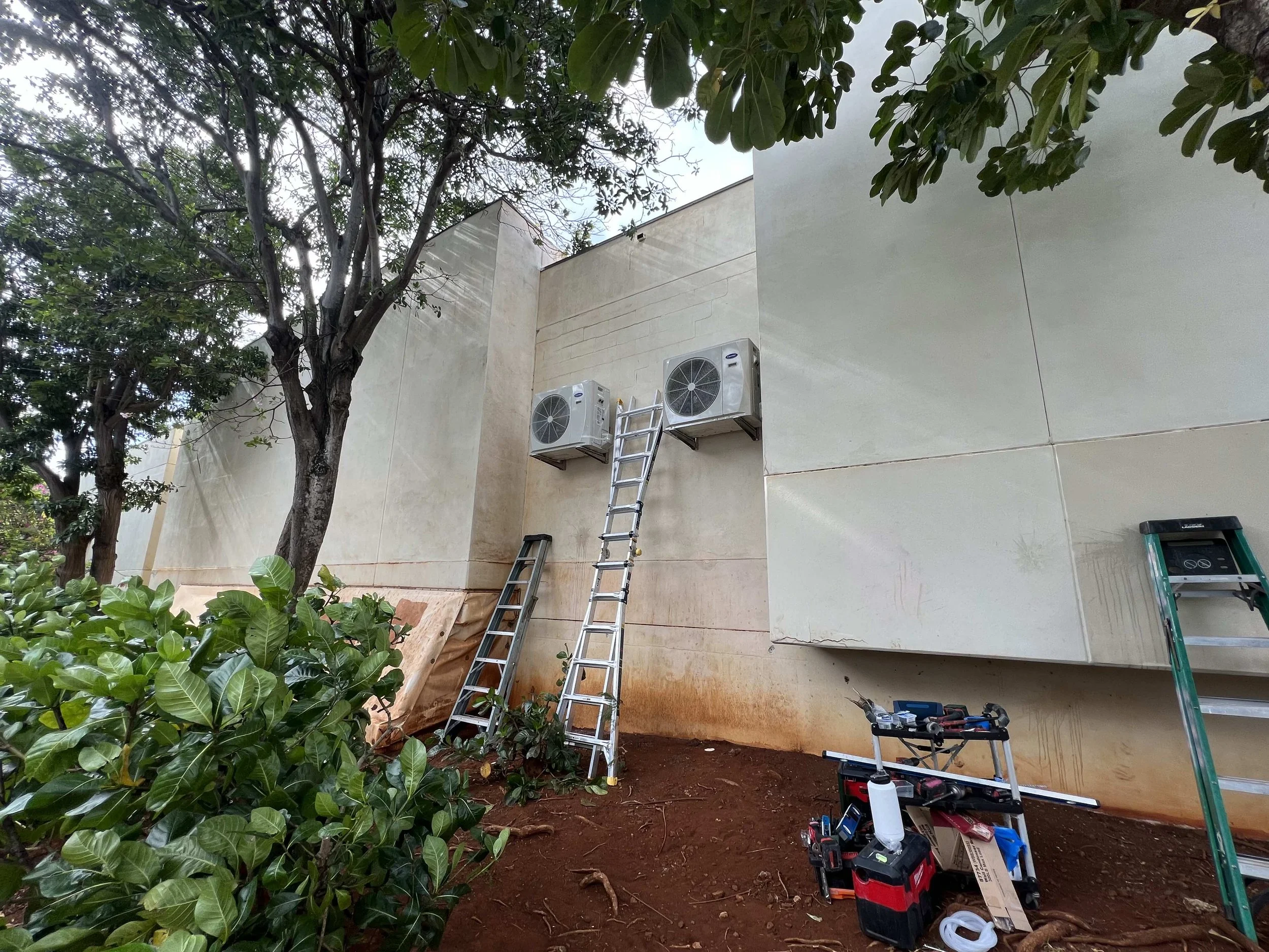 Zoomed out of two outdoor AC units installed at ground level on an exterior wall.