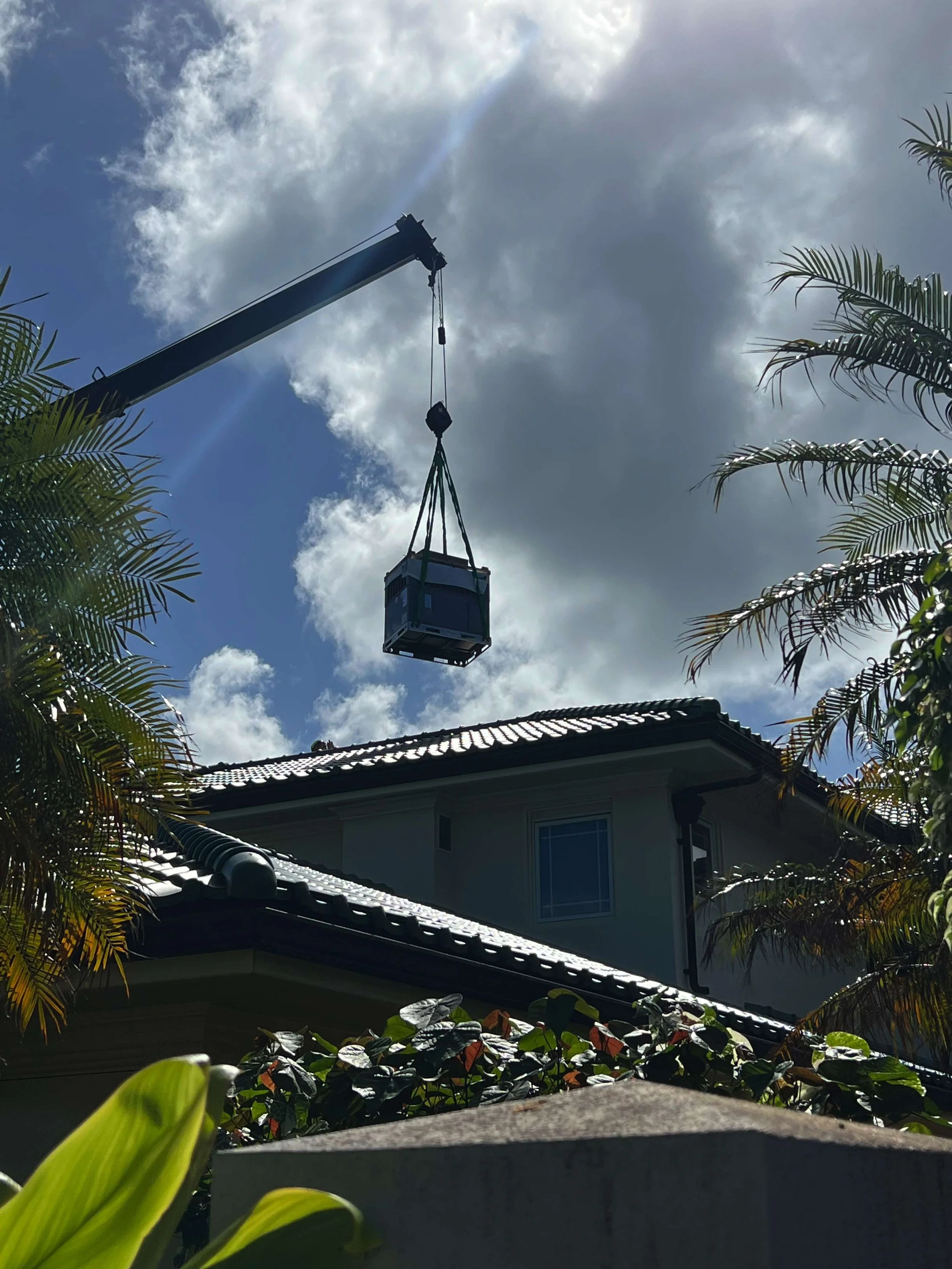 Crane hoisting a new AC system high above a roof.