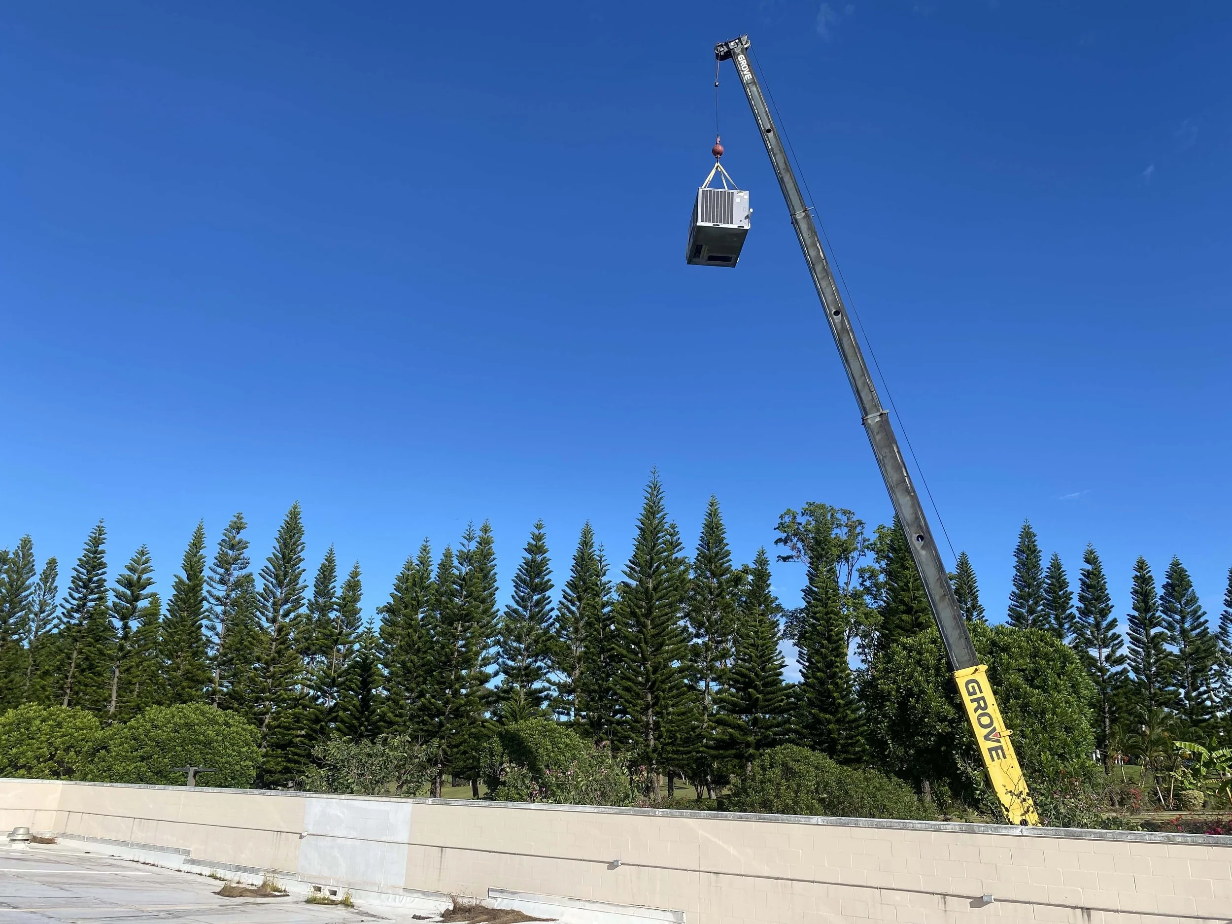 A crane lifting a new HVAC unit onto a rooftop under clear skies, November 2022.