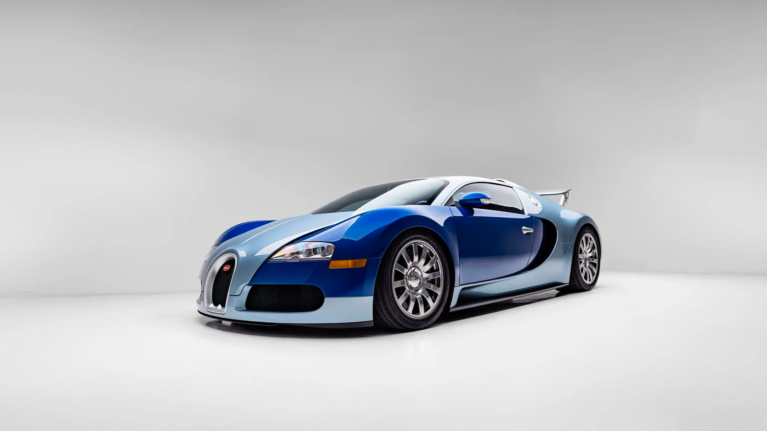 A blue and silver Bugatti sports car in a white studio setting.
