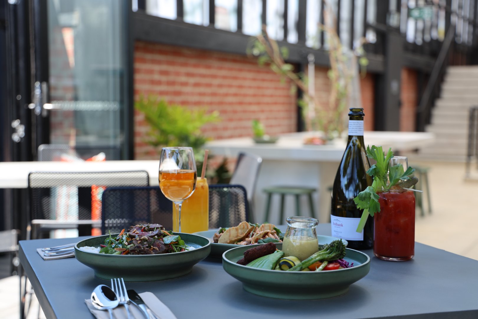 Three dishes of food and a range of drinks on a table at Little Local