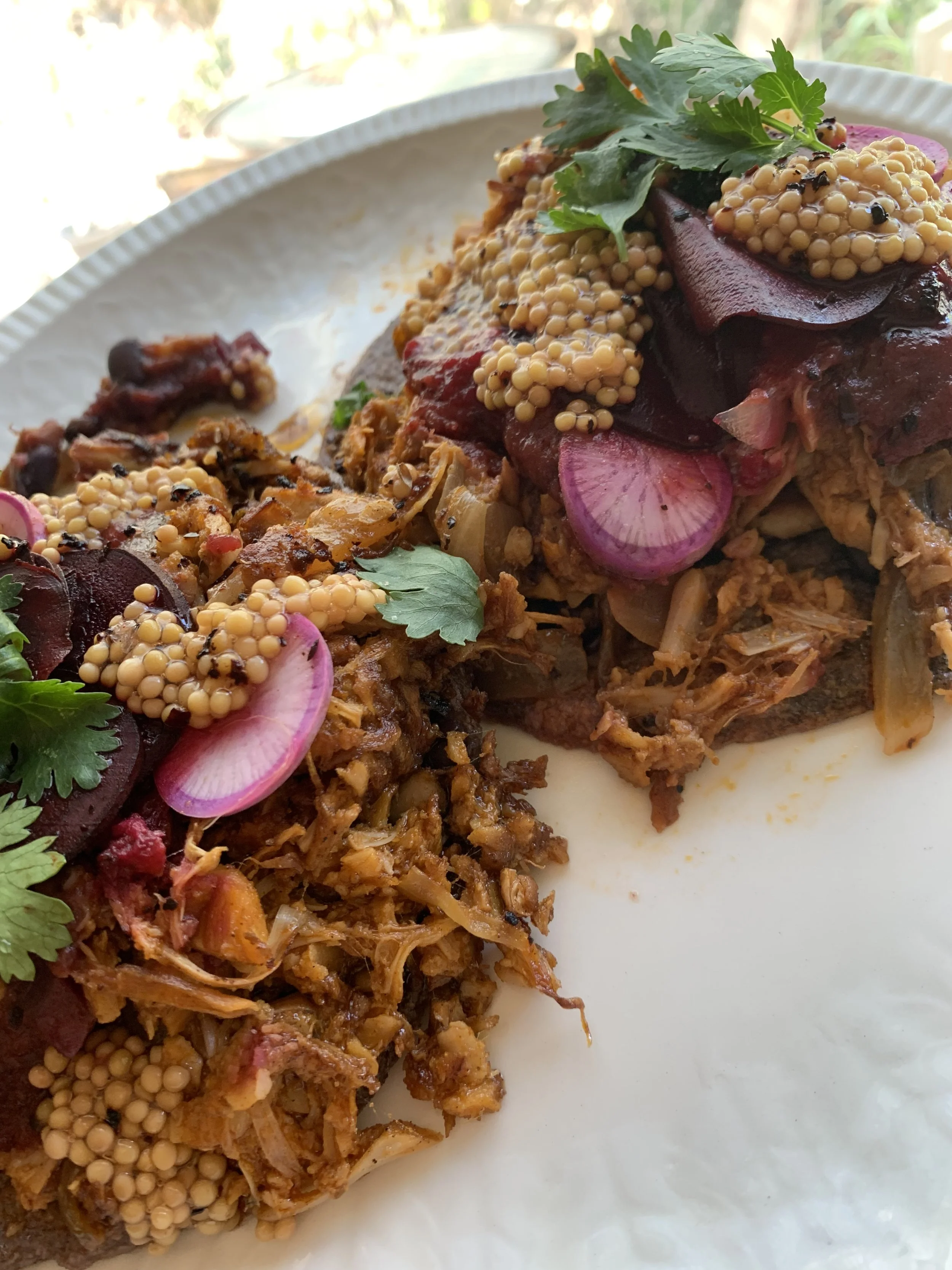 Close-up of a plate of food with shredded meat, beets, radishes, mustard seeds, and cilantro.