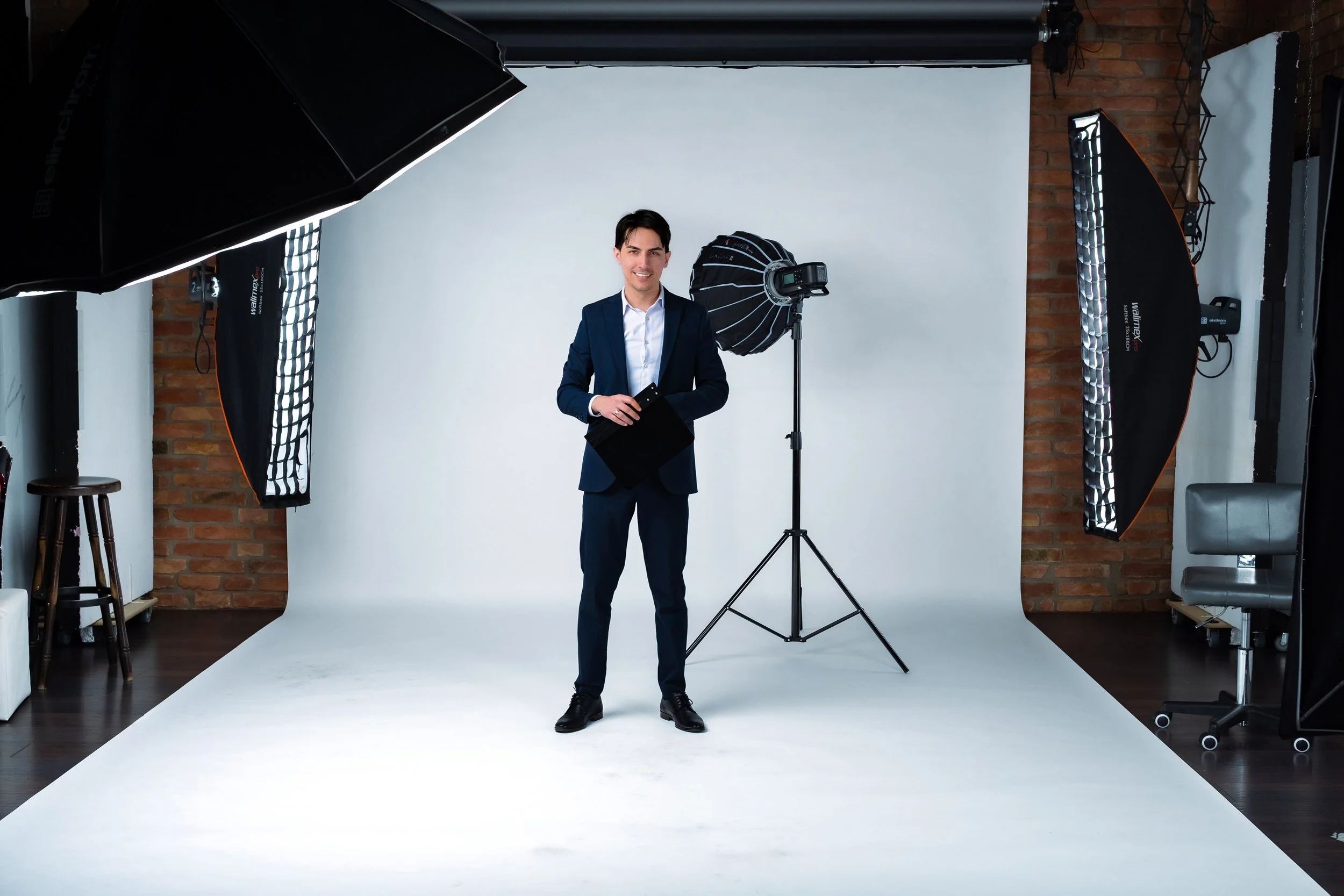 A man in a business suit standing in a photography studio with a white backdrop, surrounded by professional lighting equipment.