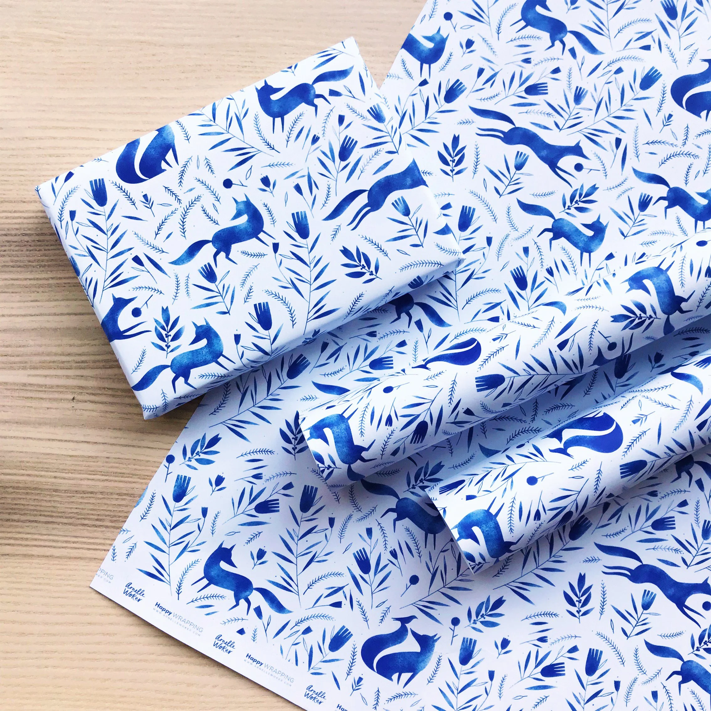 Wrapped gifts with white and blue fox and foliage wrapping paper on a light wooden surface.
