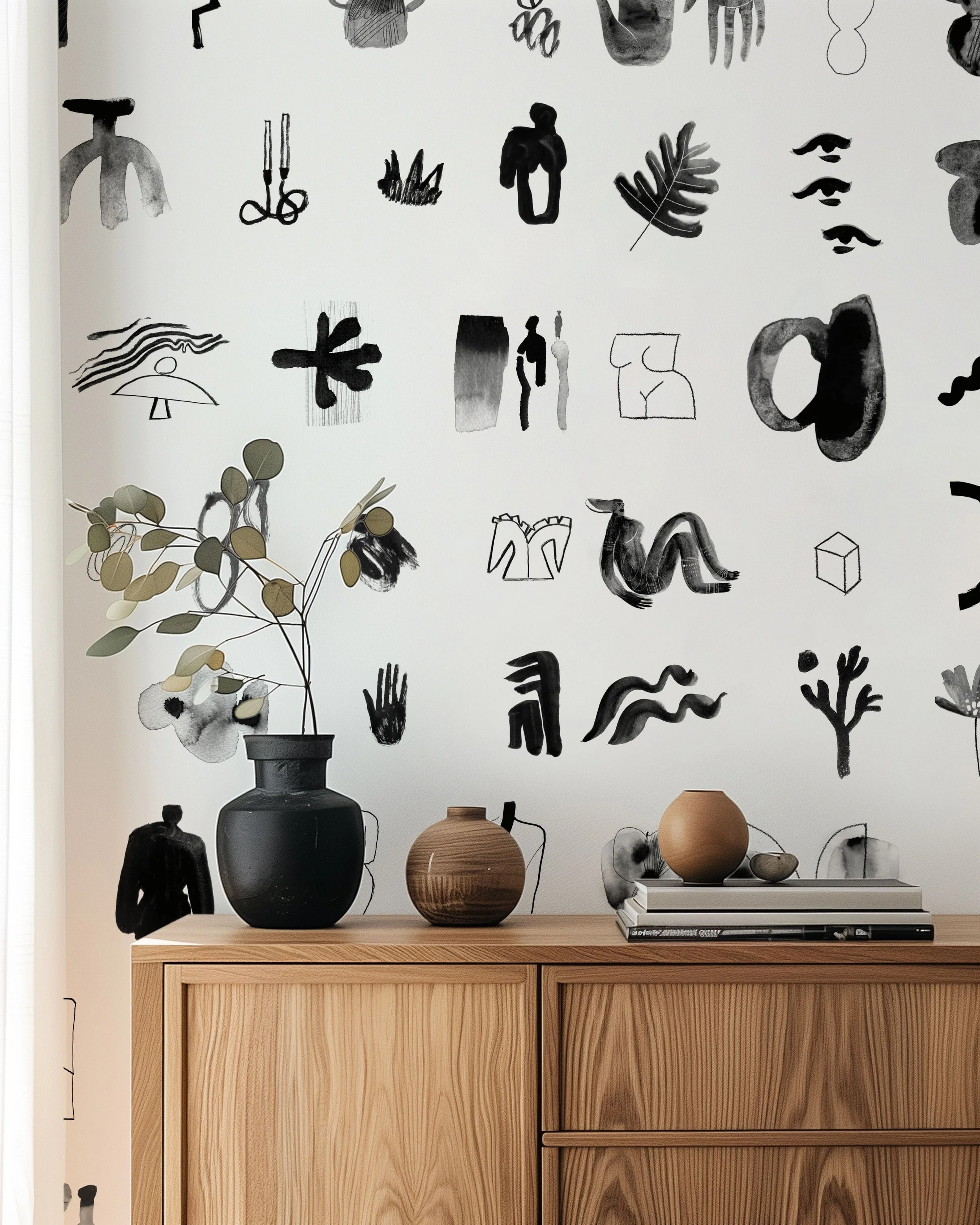 Decorative wall with black and white abstract sketches and designs, wooden sideboard with three vases and a small stack of books, and a potted plant with green leaves.