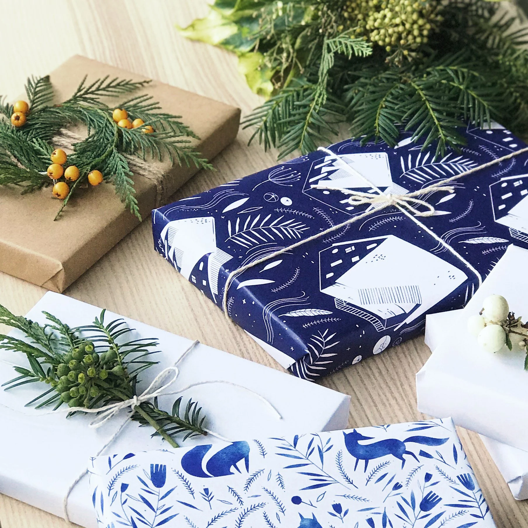 Wrapped Christmas presents on a wooden surface, decorated with greenery and berries.