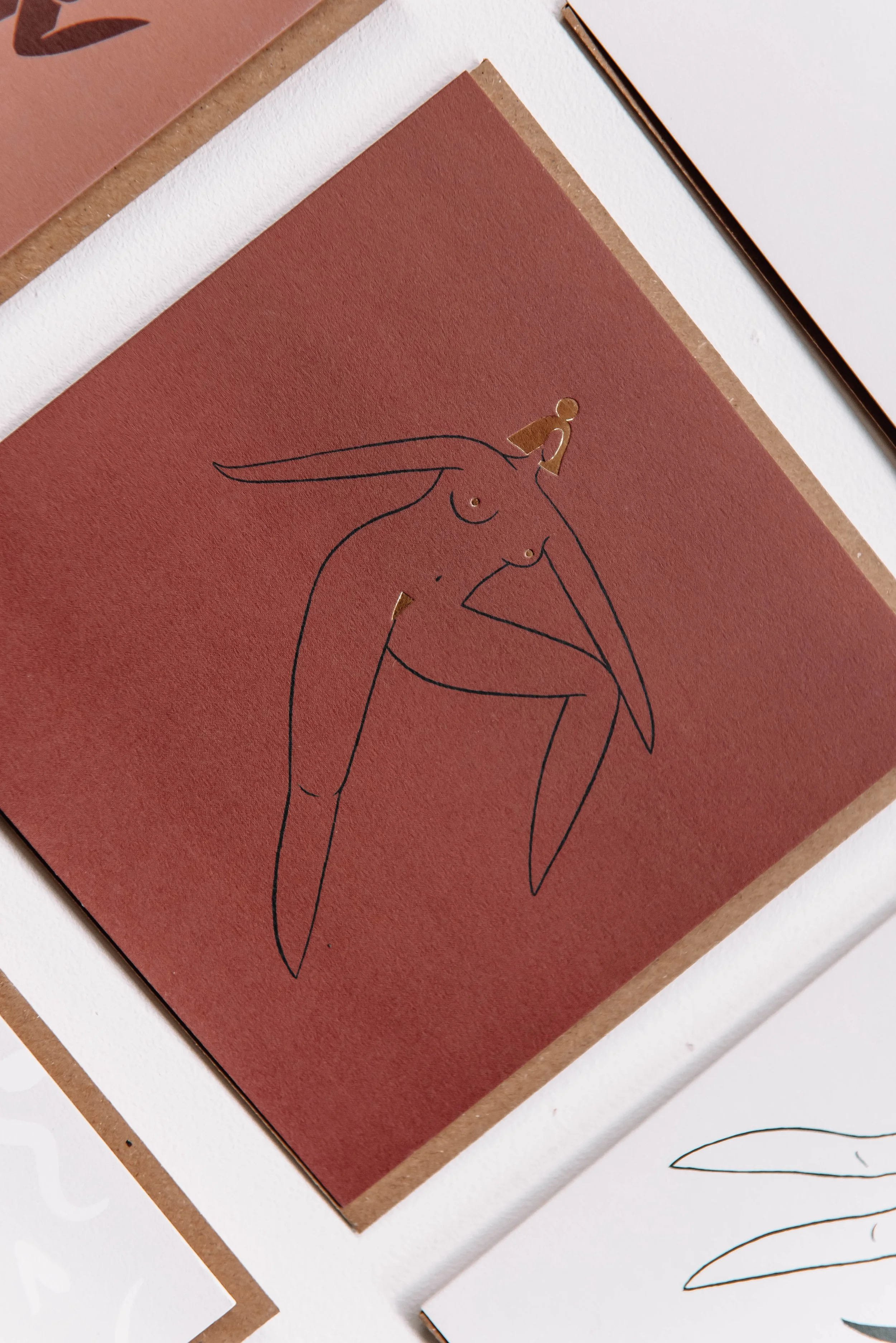 A minimalist line drawing of a woman with long hair, sitting with one leg crossed over the other, on a reddish-brown background.