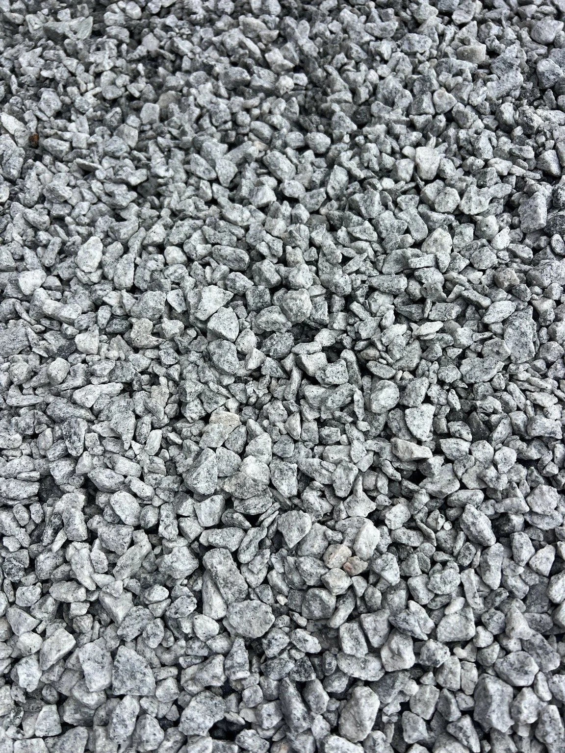 Close-up of #789 granite stone stockpile showing small angular gray stone size, texture, and natural color variation.