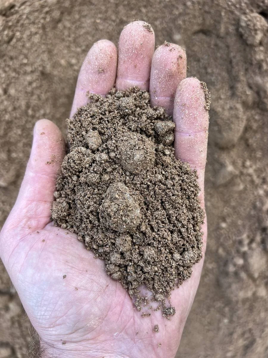 Hand holding sandy fill clay to show its fine texture, moisture, small particles, and compacted soil clumps.