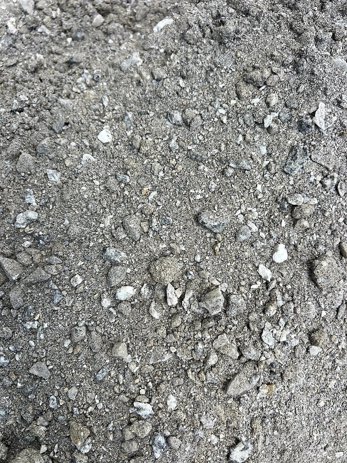 Stockpile of granite screenings containing occasional small granite rock chips, illustrating the natural variation of crushed granite material.