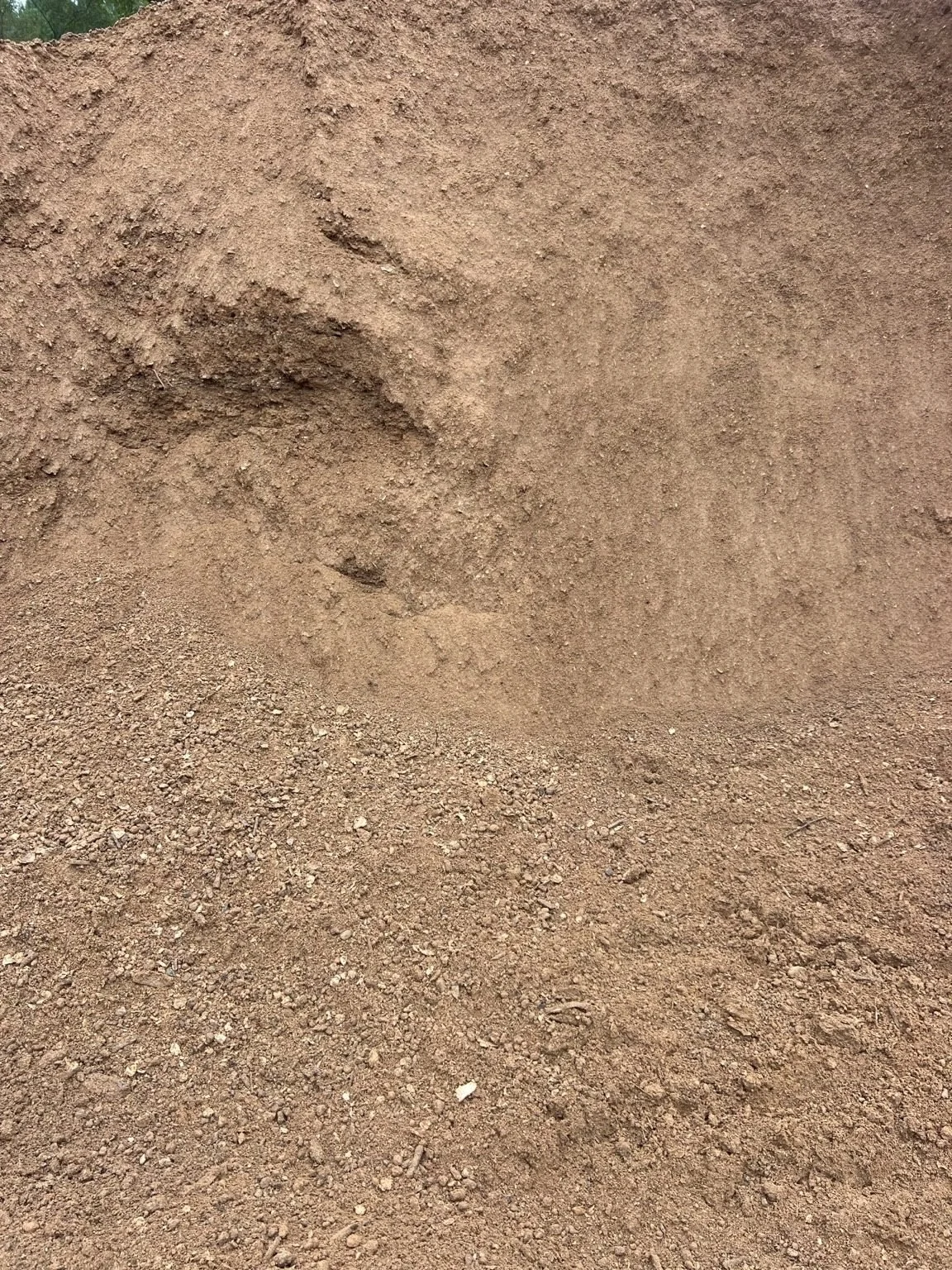 Pile of screened Sandy Loam Topsoil showing brown soil texture, small stones, and natural material variation.