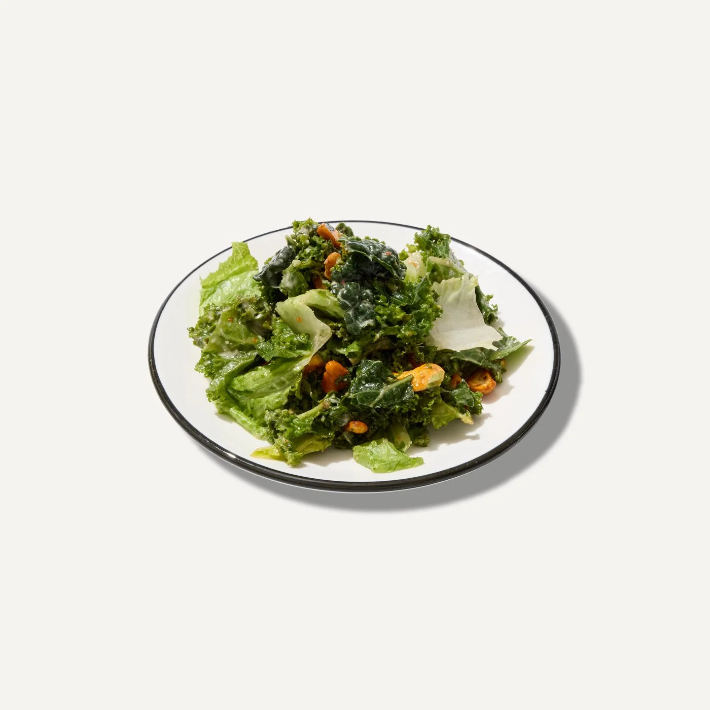 Cashew kale caesar salad with fresh greens and roasted cashews on a white plate.
