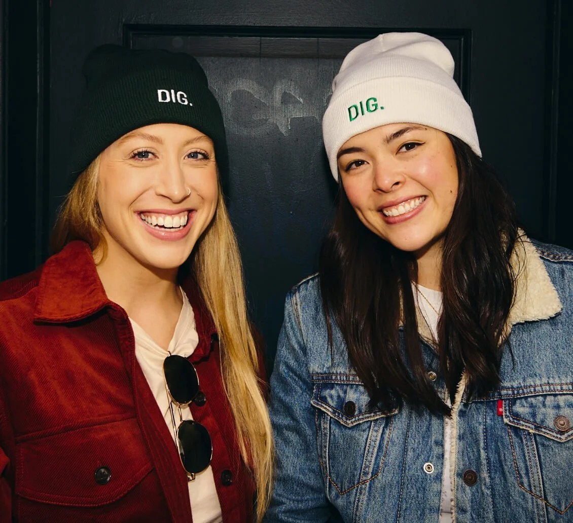 Two women wearing DIG hats smiling together, representing DIG's healthy food culture.