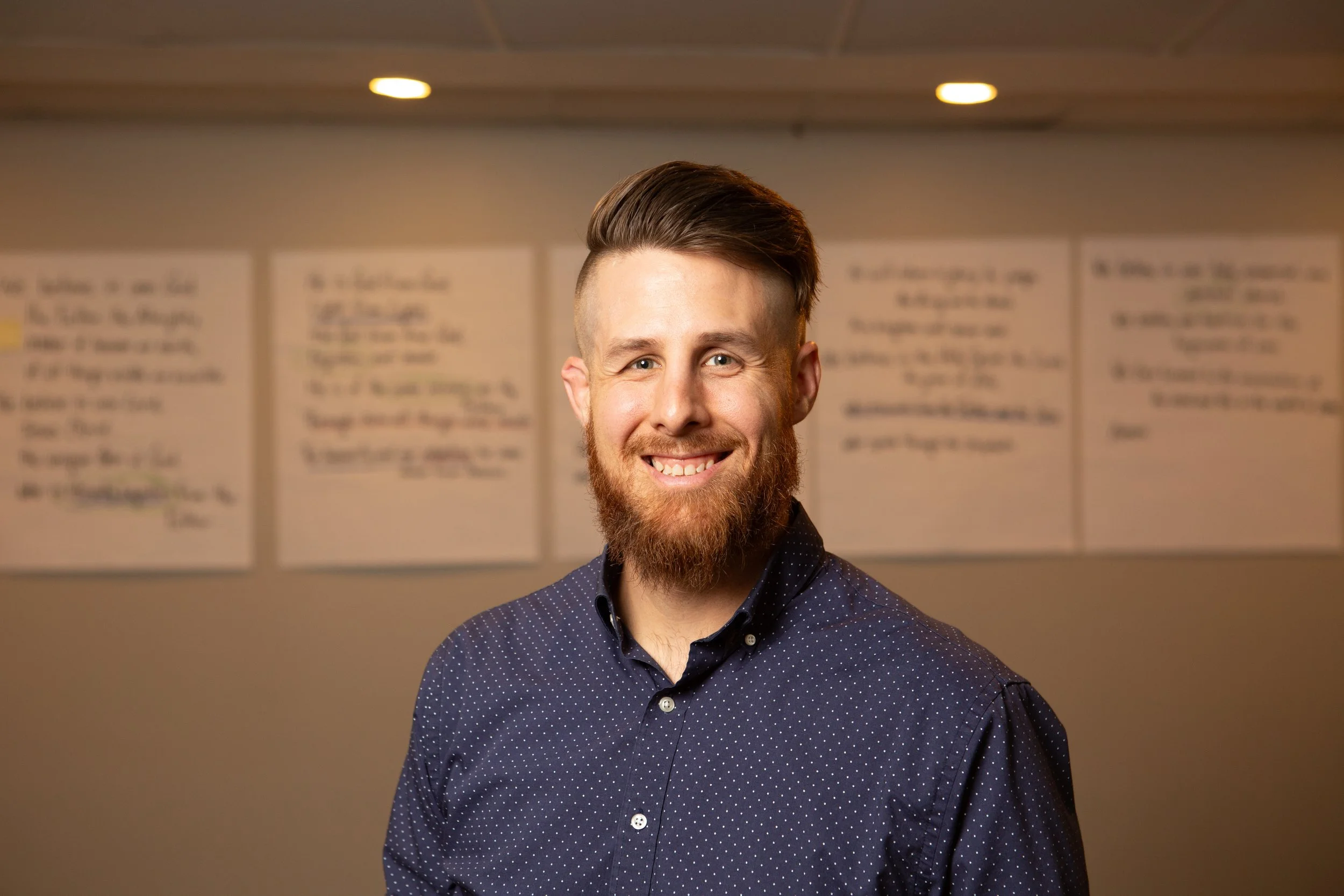 Adam Peterson, Students Pastor smiling in front of a wall with large sticky notes from different student lessons