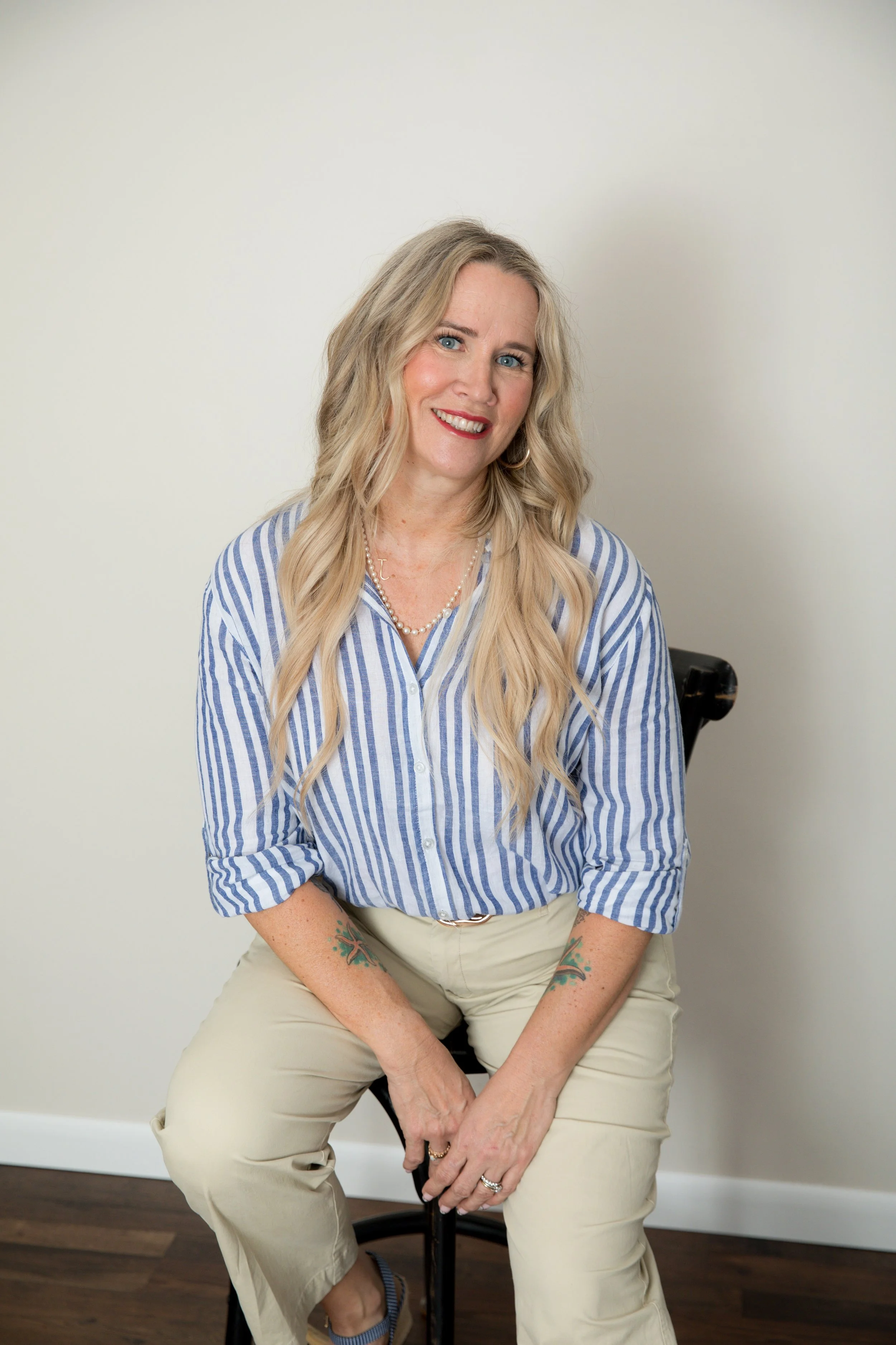 A woman with shoulder-length blonde hair wearing a white sleeveless top, smiling against a plain background.