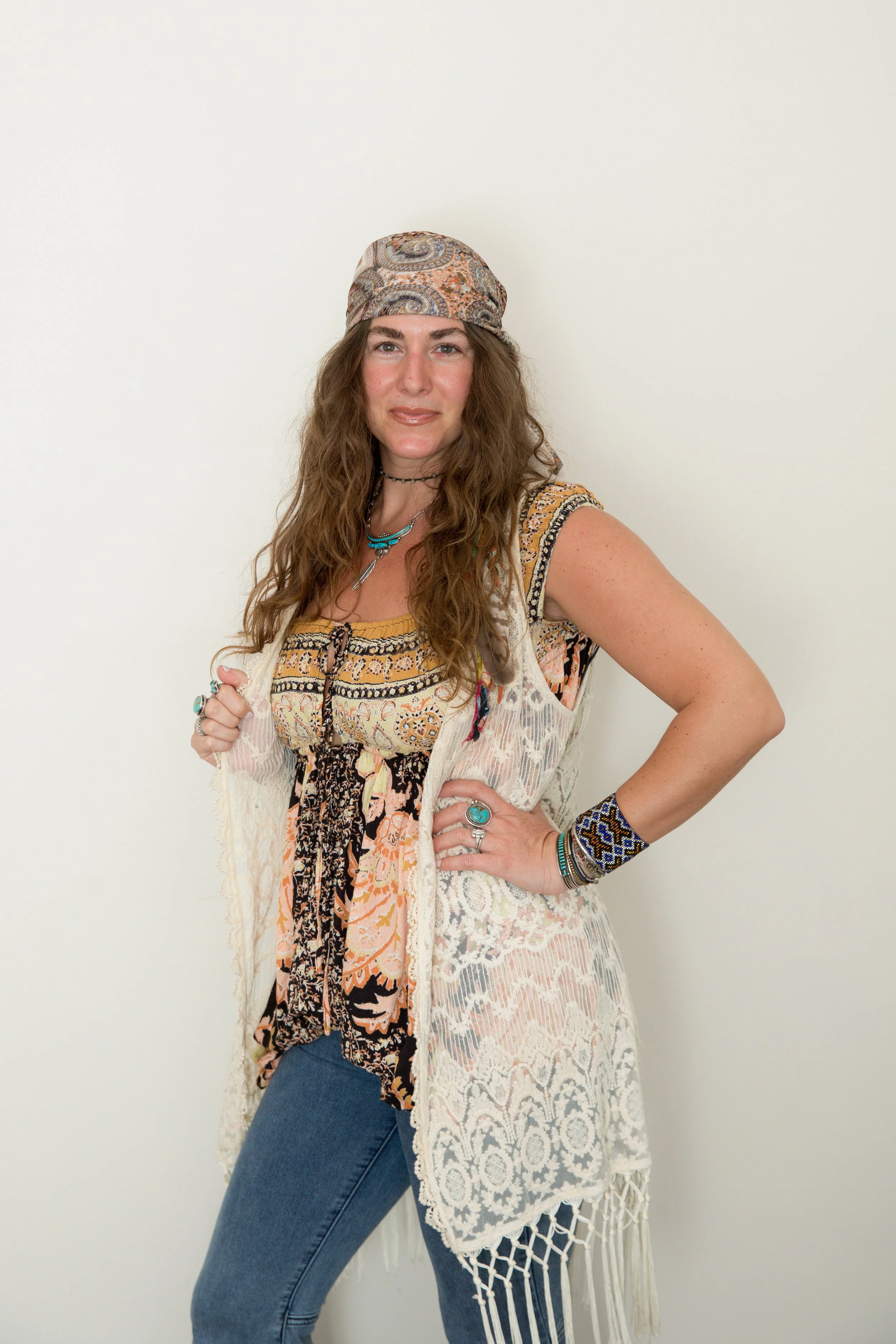 Woman with long brown hair wearing a necklace and casual clothing, smiling in front of a plain background.