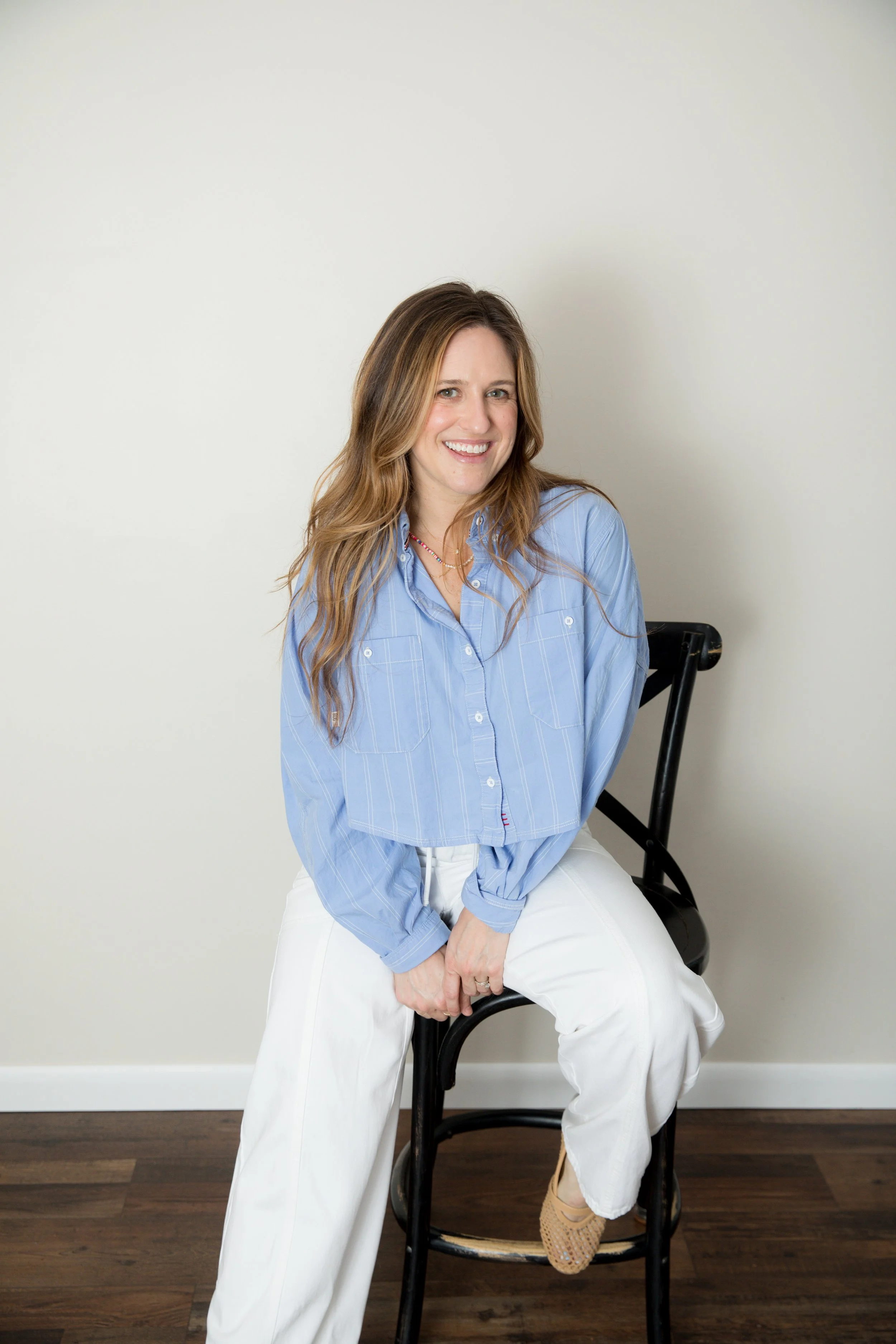 Smiling woman with long, light brown hair wearing a white blouse against a plain background.