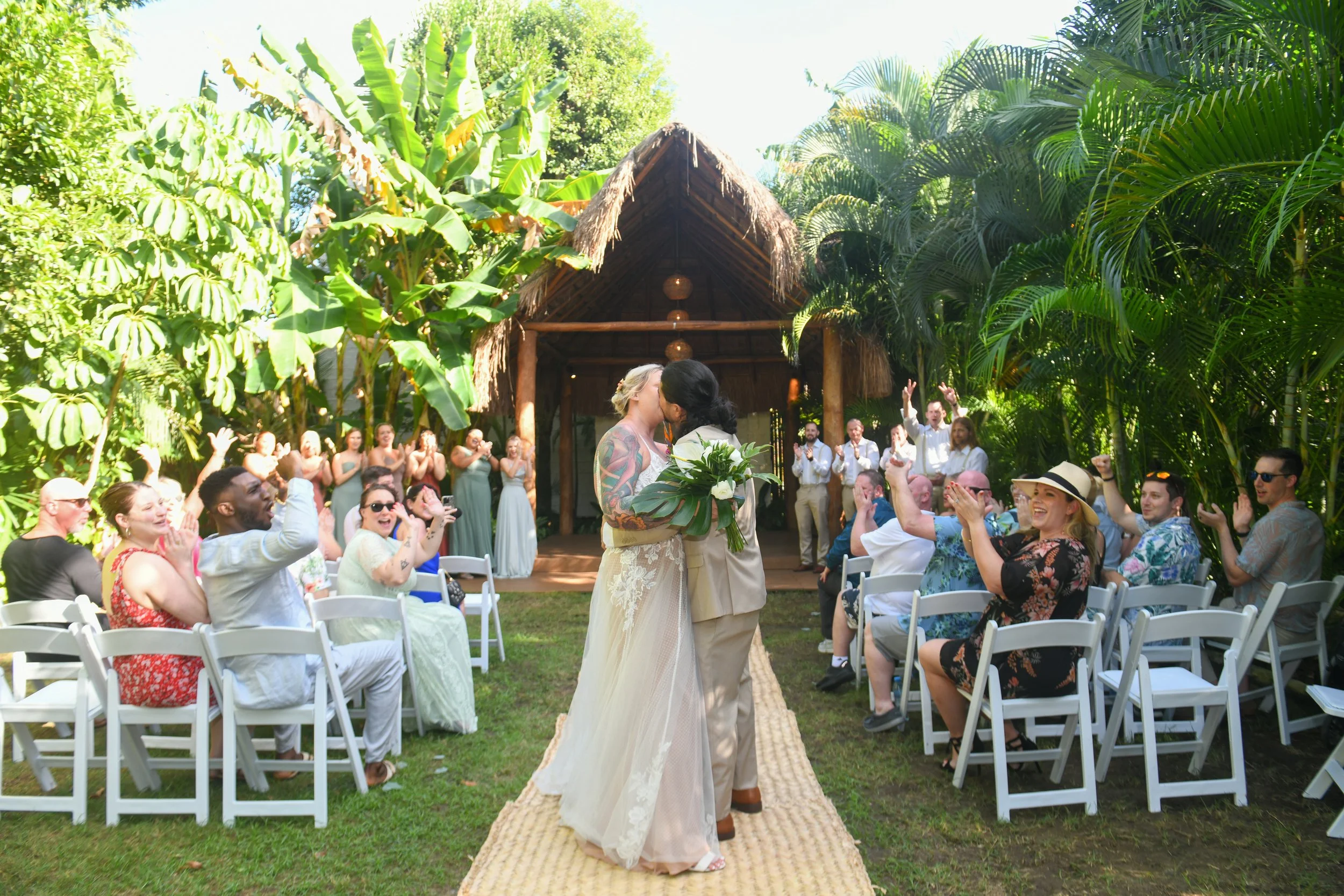 Wedding couple kiss after wedding ceremony with guests seated and clapping.  Dreams Tulum, Mexico
