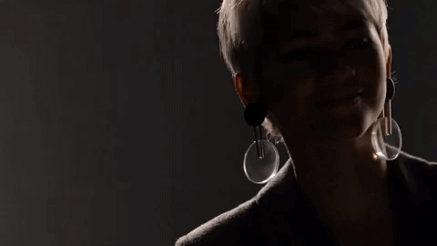 Animated gif of Zendaya smiling and wearing large circular earrings with a dark, fading light effect.