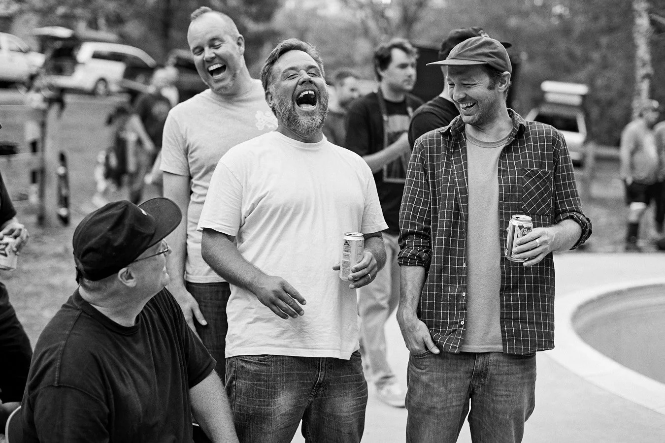 Group of middle-aged friends laughing and drinking beer at an outdoor skateboarding BBQ event