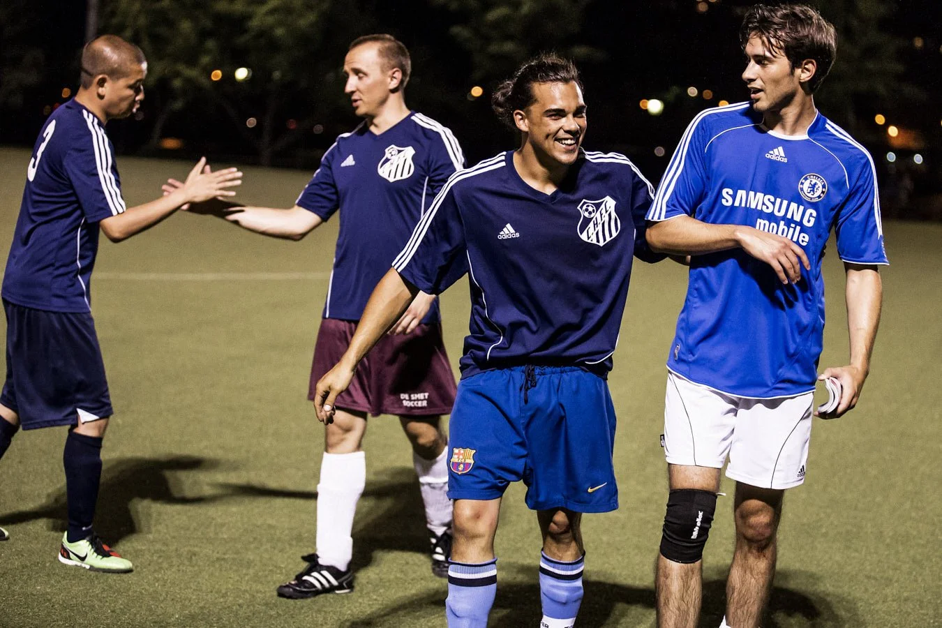 Soccer players in blue jerseys celebrating with high-fives after a game on the field.